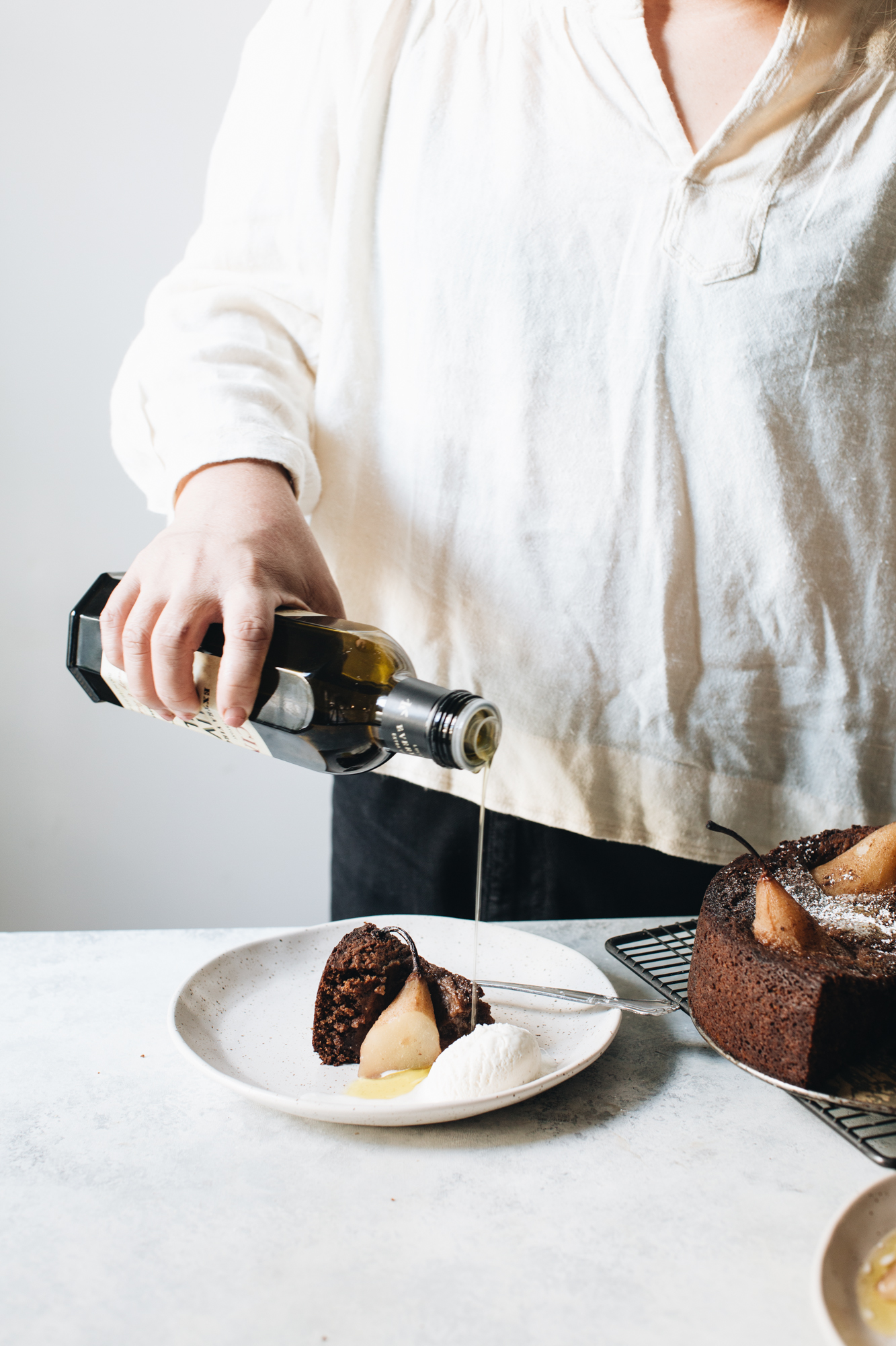 Person pouring liquid over chocolate cake with pears and ice cream.
