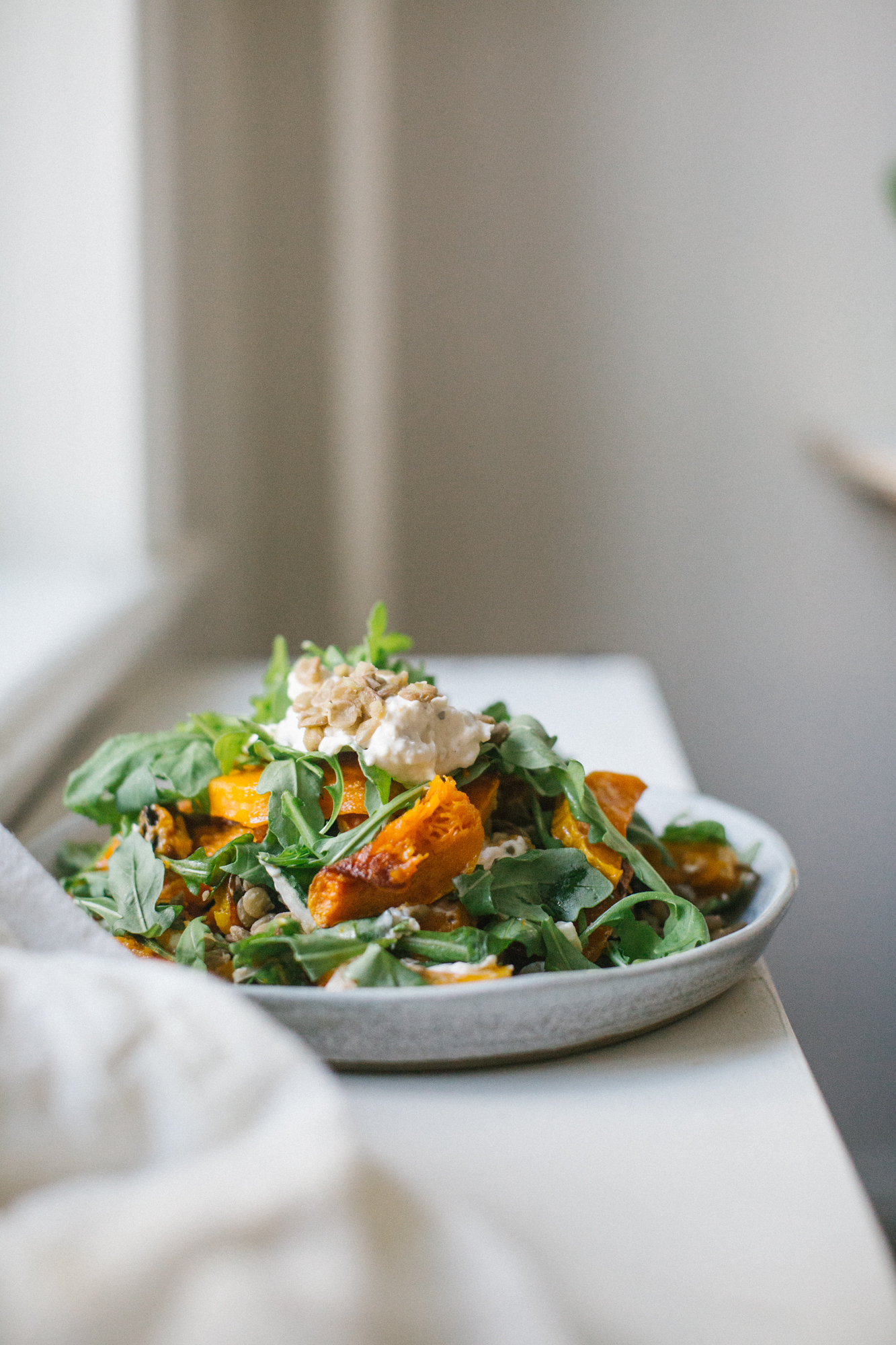 A plate of arugula salad with roasted squash, topped with ricotta cheese and seeds.