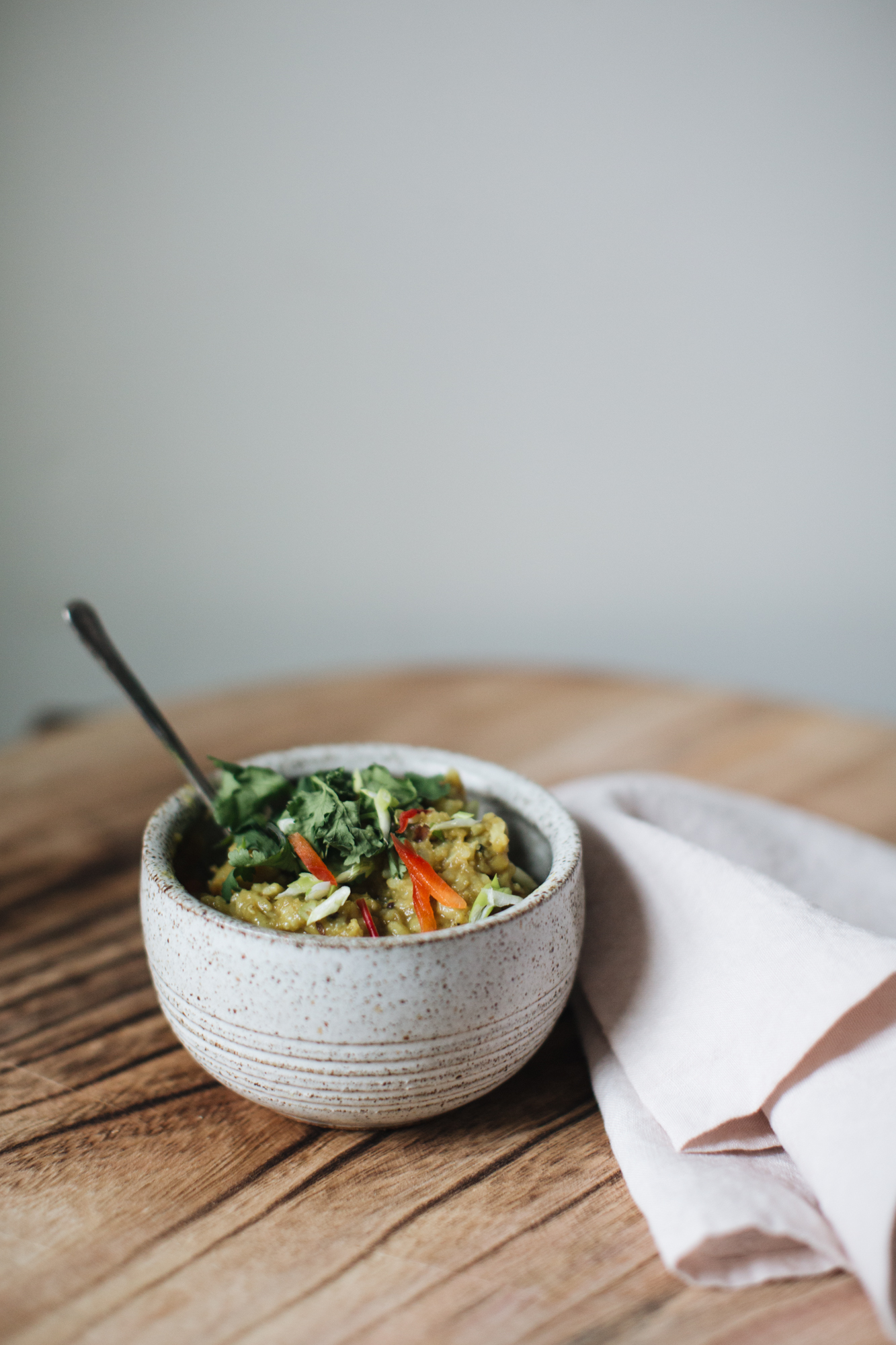 Ceramic bowl with quinoa salad and vegetables on wooden table, cloth napkin beside it.
