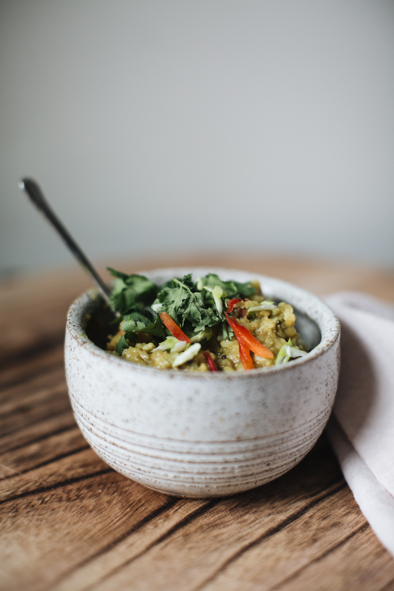 Bowl of savory oatmeal topped with vegetables and herbs on a wooden table.