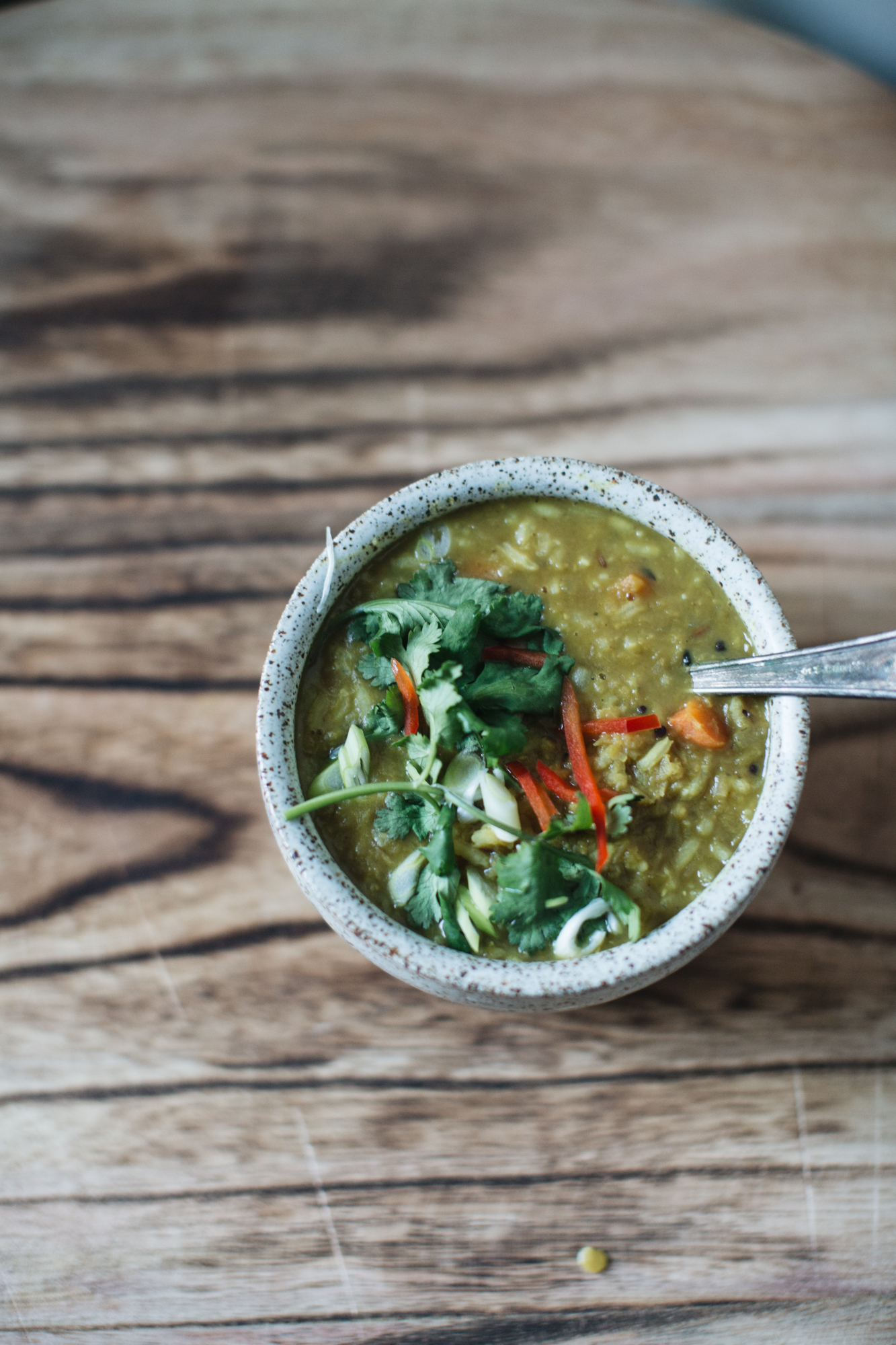 A bowl of vegetable soup topped with cilantro and sliced red peppers on a wooden table.