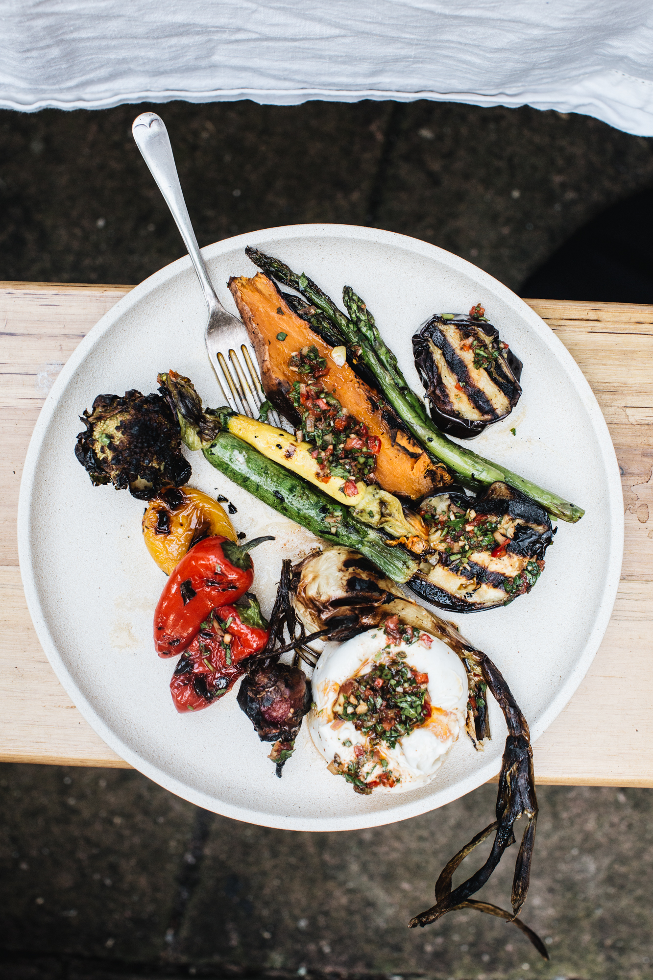 Grilled vegetables on a plate including zucchini, asparagus, bell peppers, and a burrata cheese, garnished with herbs.