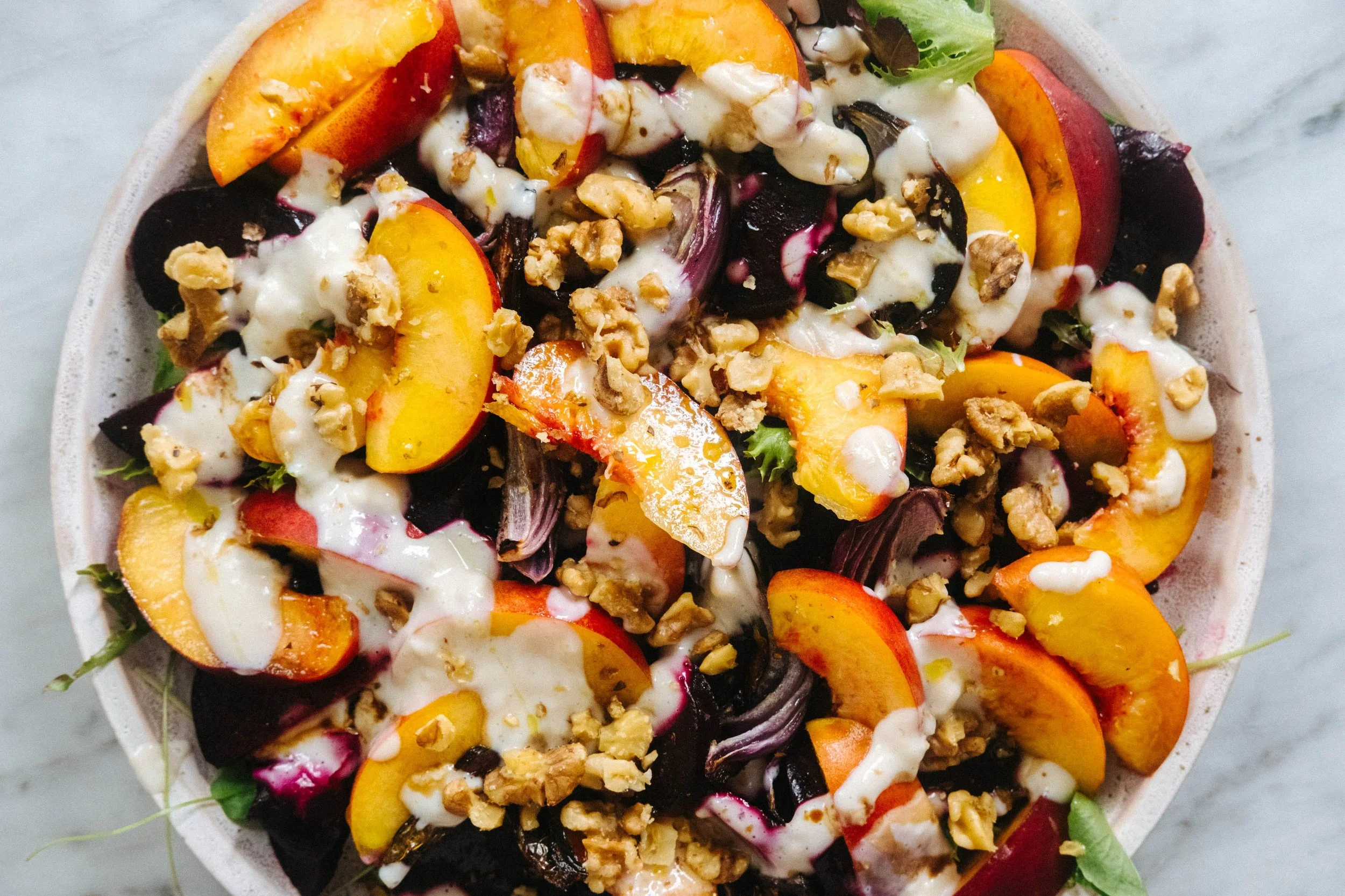 Colorful fruit salad with peaches, plums, and mixed greens topped with creamy dressing and chopped nuts.