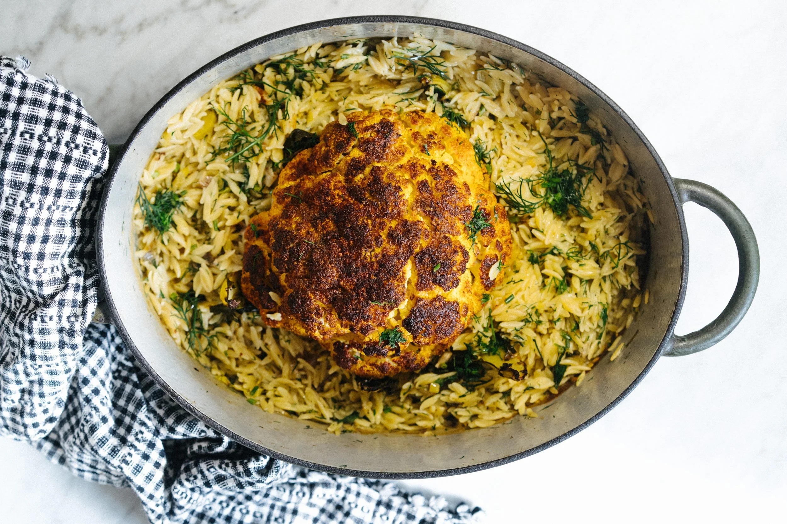 Roasted cauliflower atop orzo pasta with herbs in a pot.