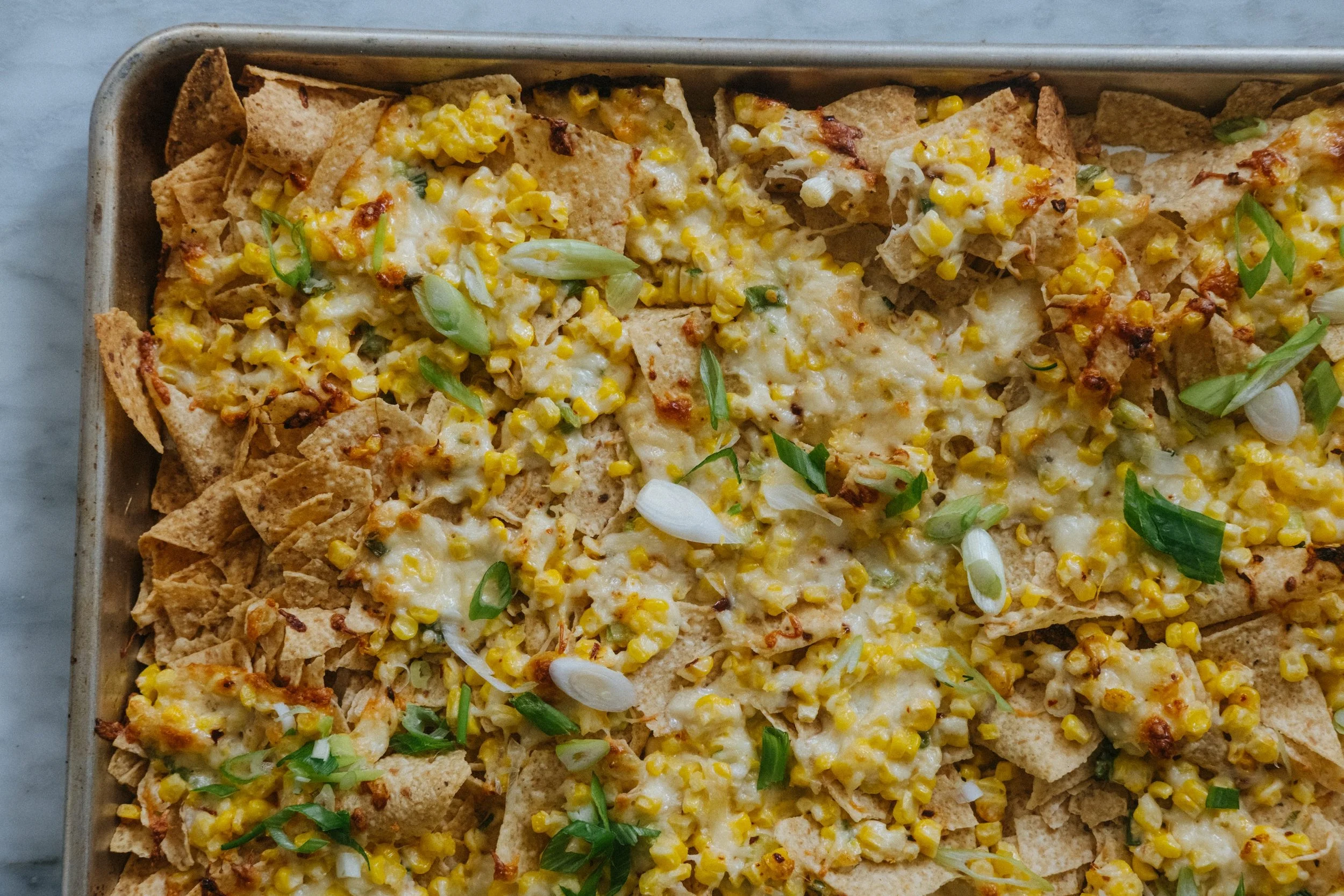 Baked nachos with melted cheese, corn, and chopped green onions on a tray.