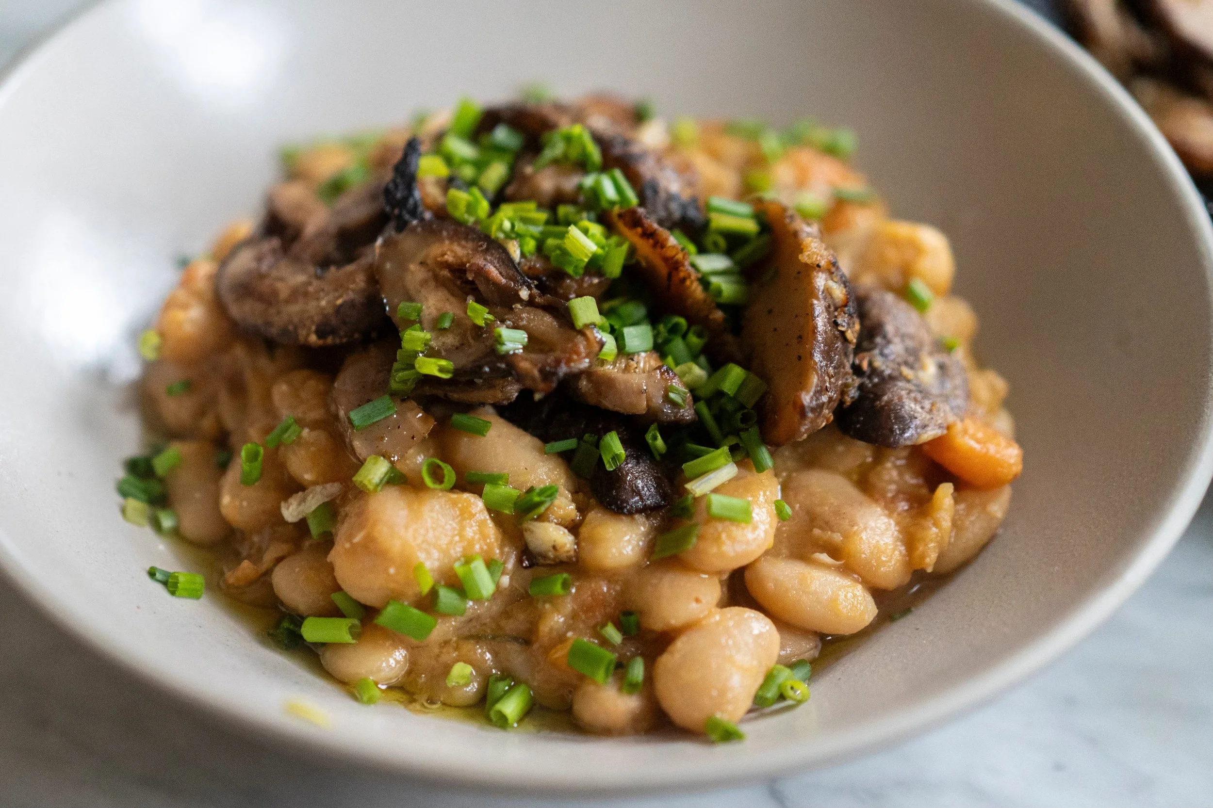 A bowl with cooked white beans topped with sautéed mushrooms, garnished with chopped green onions.