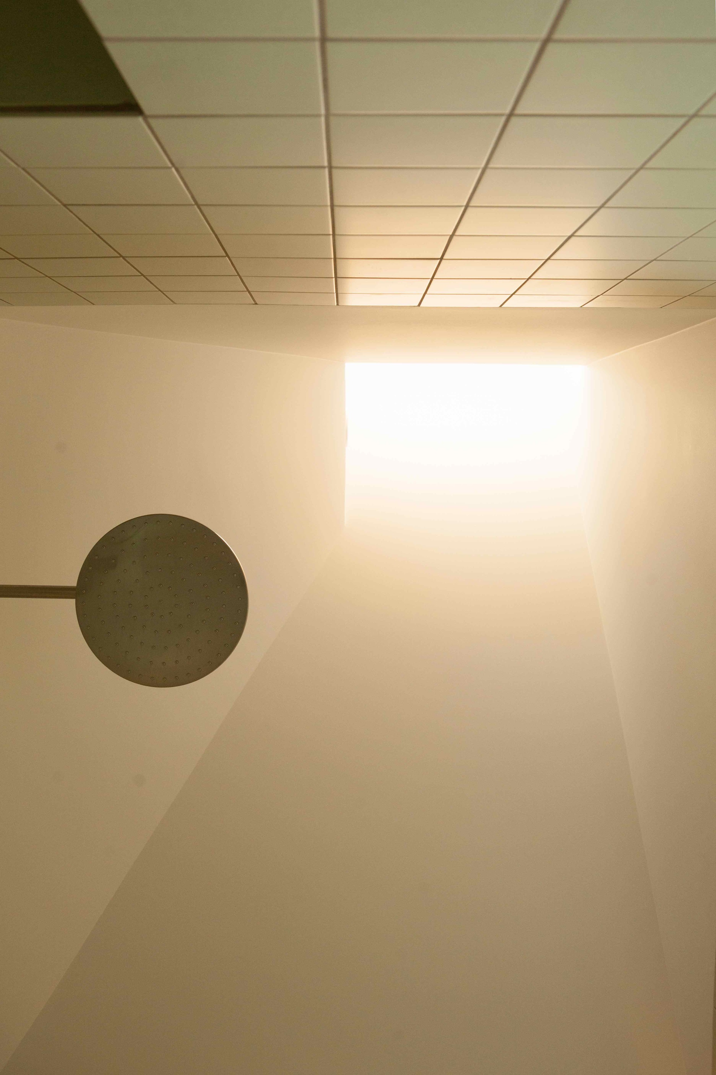 Above the tile and the showerhead, angled drywall tapers into a skylight 12 feet above the shower.