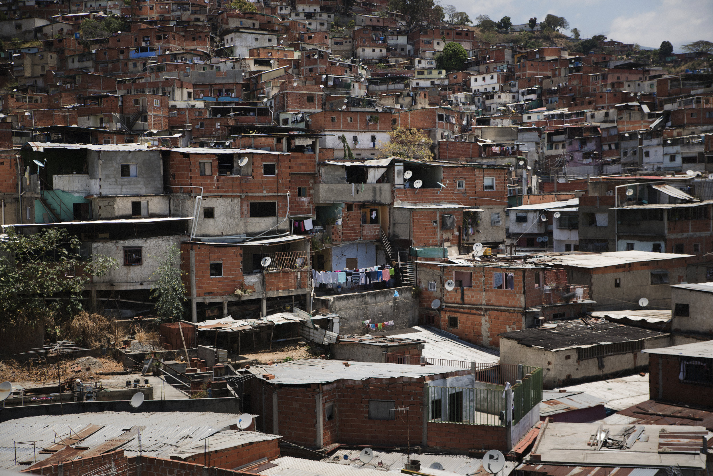 Different hills surround the perimeters of Caracas. They are slums built at the edge of any urbanistic plan by the poorest families that didn't find a better place to start a new life. Houses raised without a license, buildings devoid of the minimum security rule, constructions in wood, brass and bricks. Homes in precarious conditions, threatened by the landslides caused by rains. Thousands of people living in these houses, lacking any coziness. According to the INE, in 2011 in the Petare parish, for example, there were over 372,616 people living there. The projection for 2025 is of 465,713 inhabitants. It is the most popular slum in Caracas. Los distintos cerros recorren el perímetro de Caracas. Son barrios construidos al margen de cualquier plan urbanístico por las familias más humildes que no encontraron un lugar mejor para empezar una nueva vida. Casas levantadas sin licencia, edificaciones desprovistas de la más mínima regla de seguridad, construcciones forjadas en tablas de madera, latón y ladrillo. Hogares precarios, amenazados por corrimientos de tierra provocados por las lluvias. Miles de personas viven en estas casas carentes de la más mínima comodidad. Según el INE, en 2011 en la parroquia Petare, por ejemplo, vivían 372.616 habitantes. La proyección para el 2025 es de 465.713 personas. Es el barrio popular más grande de Caracas. Caracas (April, 2018).