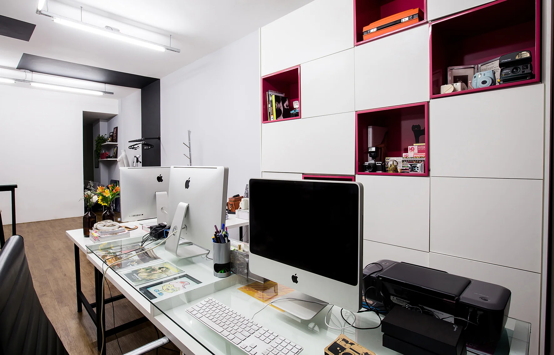 Escritório com armários de mdf branco e nichos com laca brilhante rosa, mesas com estrutura metálica e tampos de mdf e vidro.