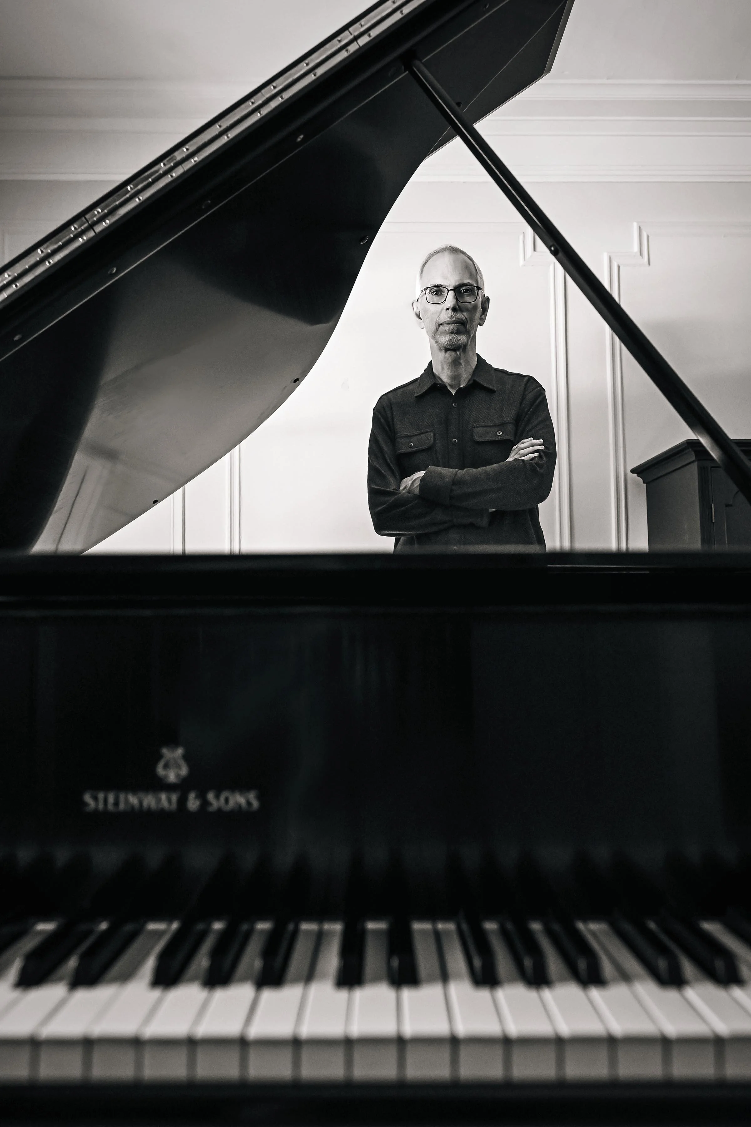 View from inside a grand piano, looking down onto the keyboard with a person standing behind the open lid of the piano.