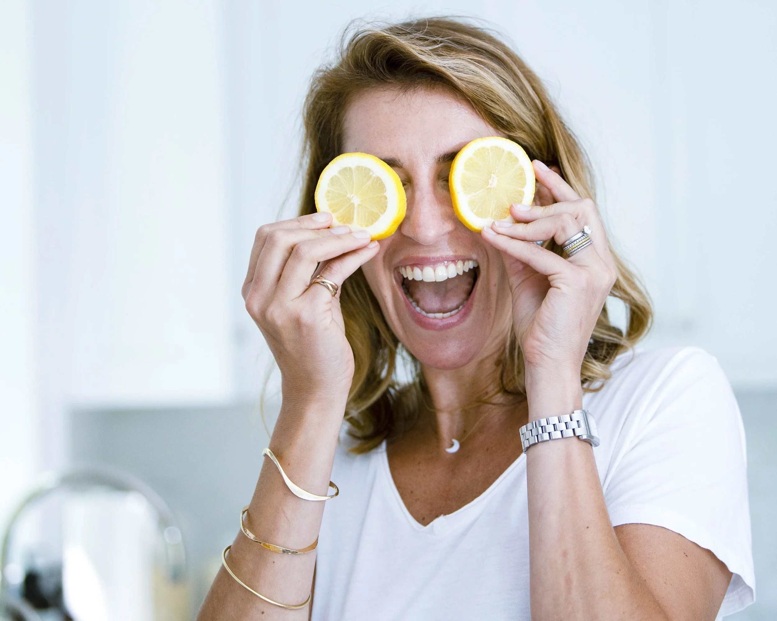 Woman with wavy red hair smiling and holding lemon slices in front of her eyes.