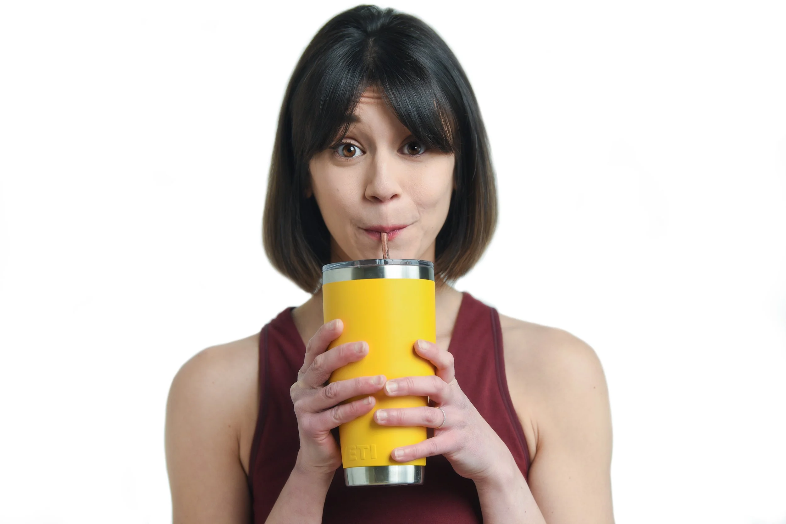 A woman with shoulder-length dark hair sipping a drink through a straw from a yellow tumbler