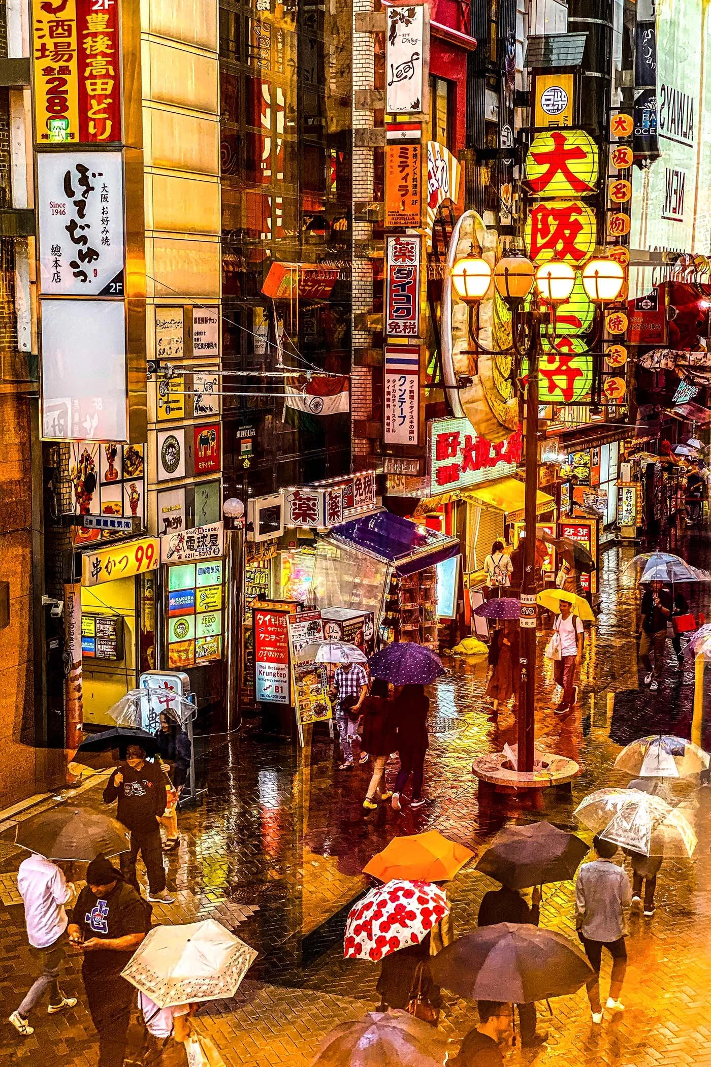A busy city street scene in Japan during rainy weather, with numerous pedestrians holding umbrellas and walking on wet pavement. The street is filled with colorful signs and billboards, including Japanese characters and neon lights, creating a lively, vibrant atmosphere.