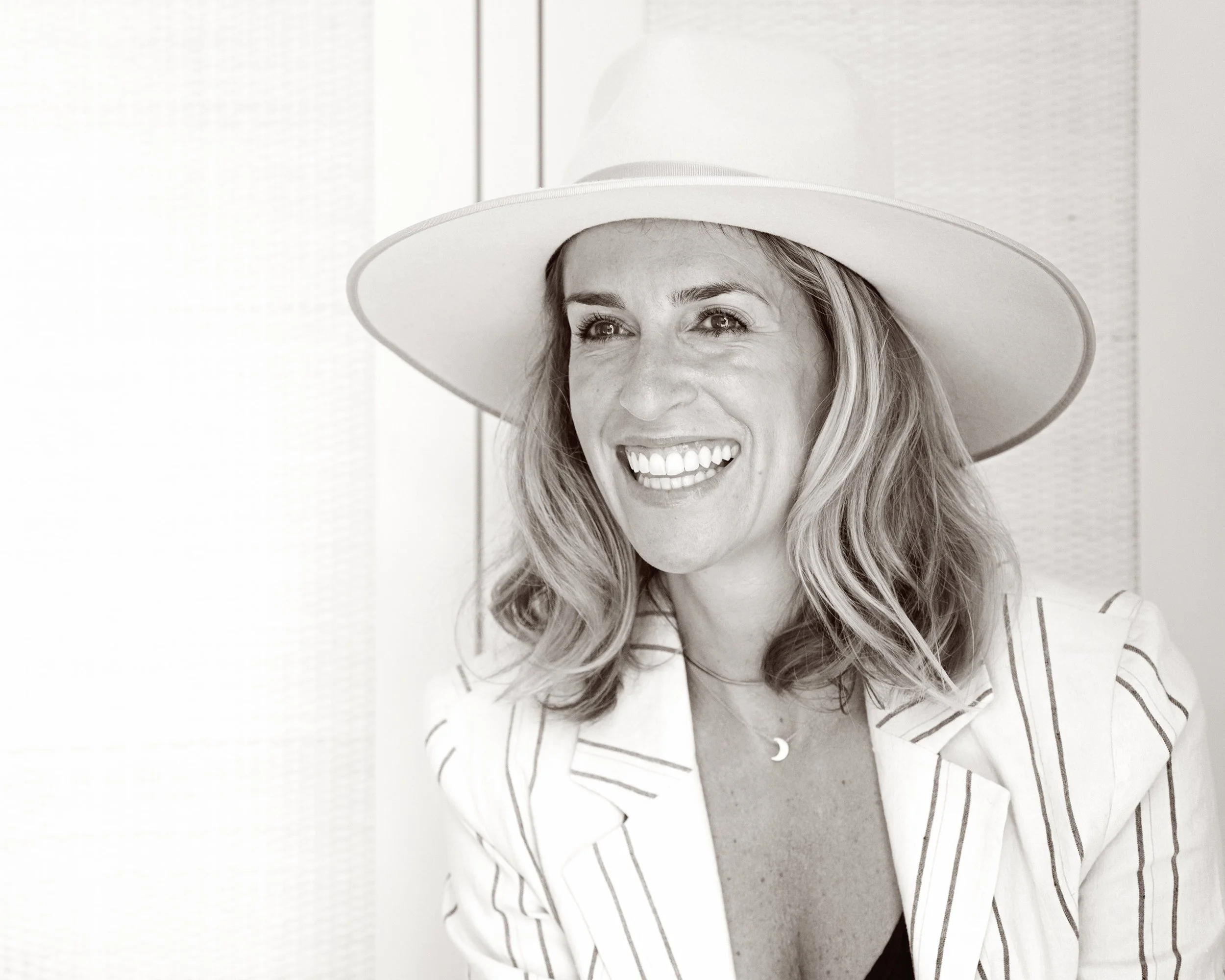 A smiling woman wearing a white wide-brimmed hat and a striped shirt.