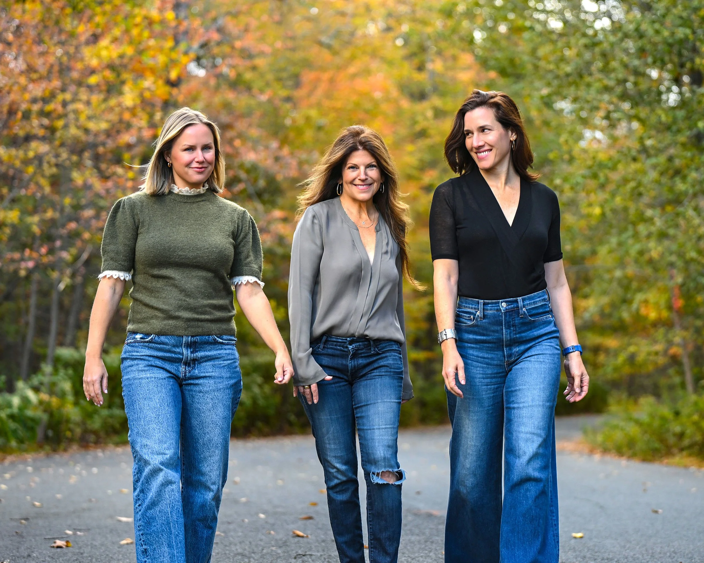 Three women walking outdoors in a park during autumn, surrounded by colorful fall foliage.