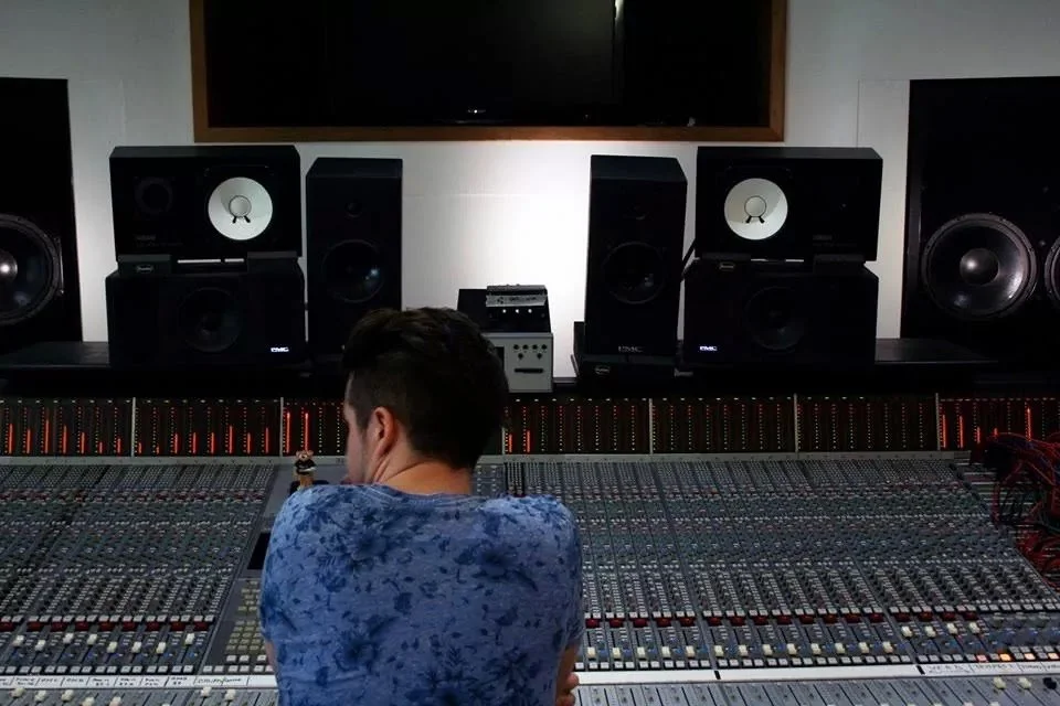 Shane Shanahan is sitting in front of Westpoint Studios SSL mixing console in Westpoint Studios, with multiple large speakers.