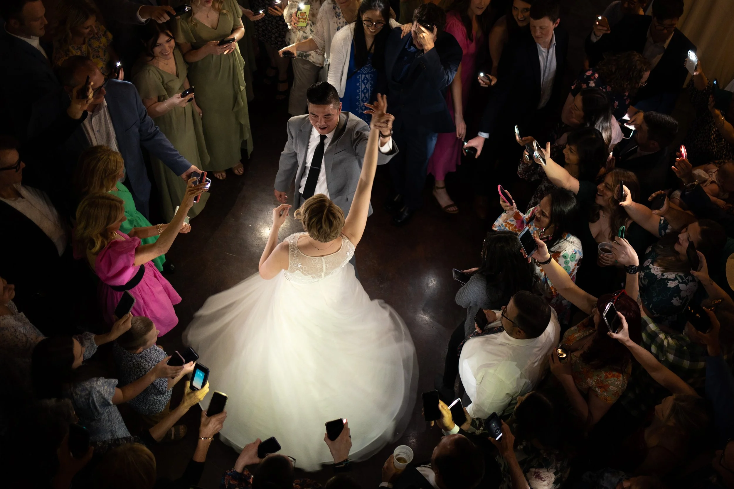 A bride and groom dancing at their wedding reception surrounded by guests taking photos.