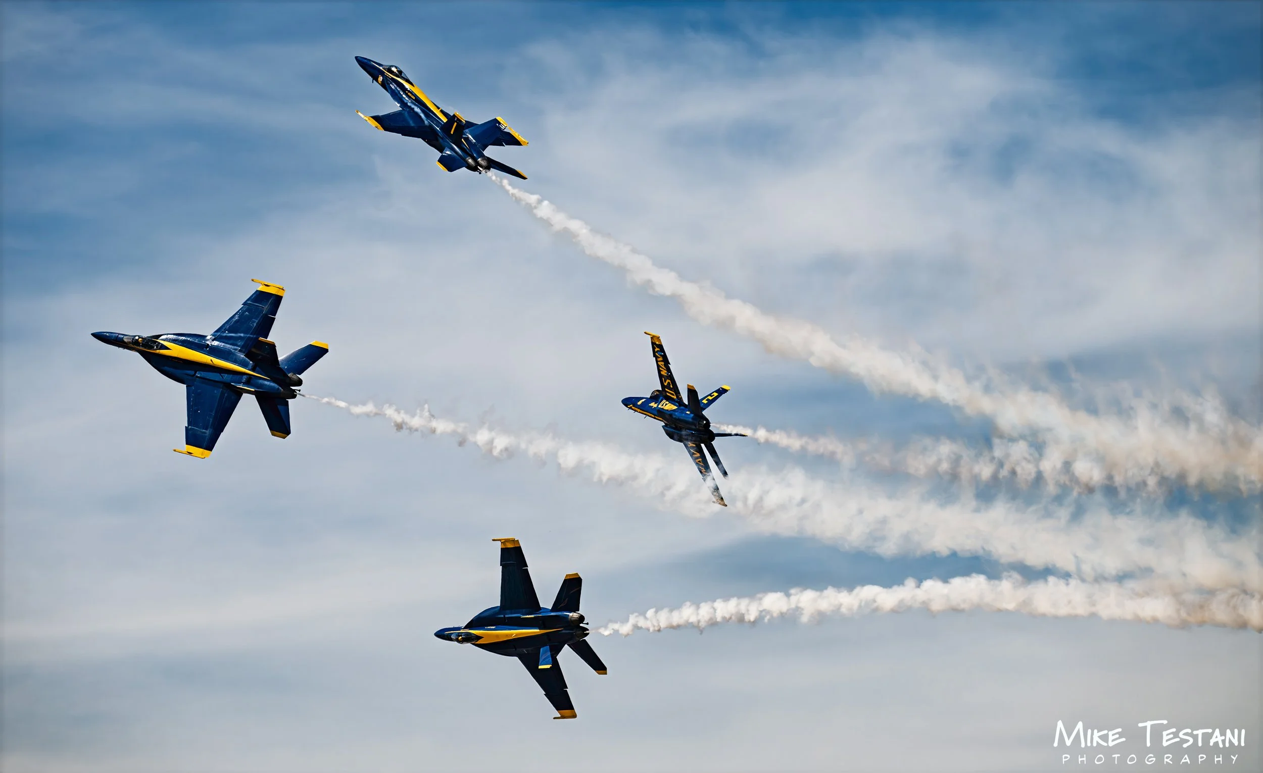 Four Blue Angels fighter jets flying in formation with smoke trails in the sky during an air show.