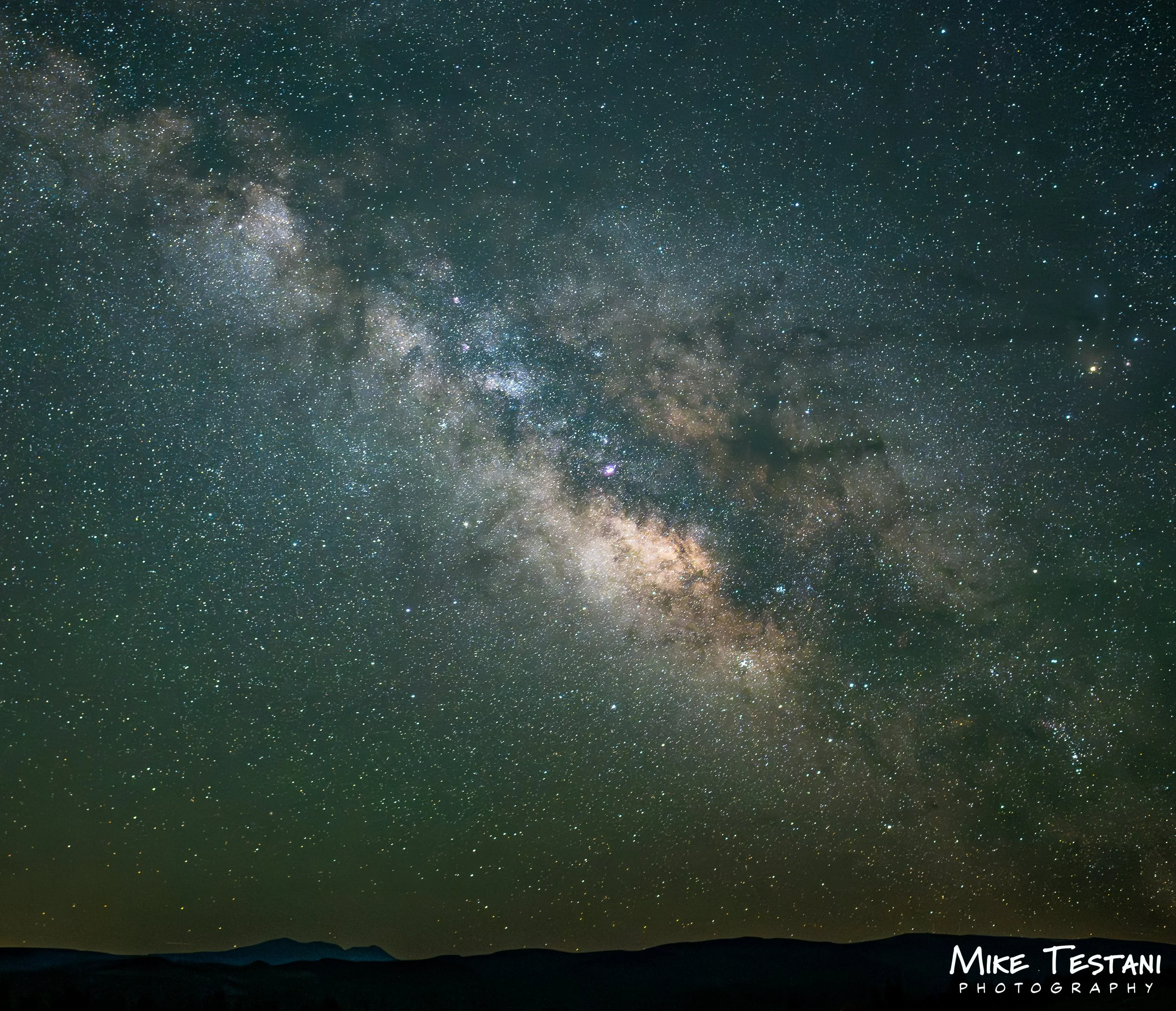 A night sky filled with countless stars and the Milky Way galaxy visible above a silhouette of mountains.