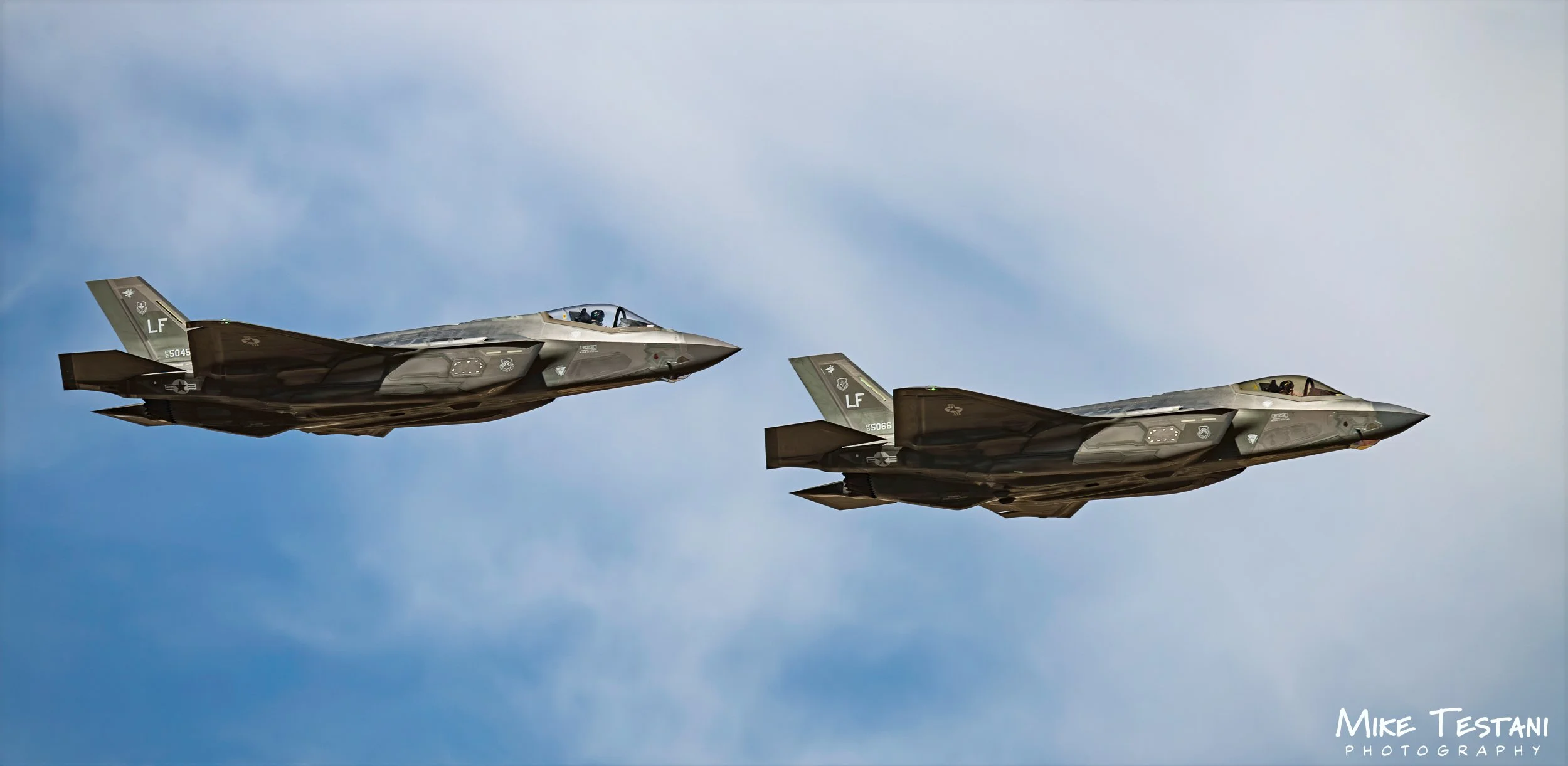 Two fighter jets flying in formation against a cloudy sky.