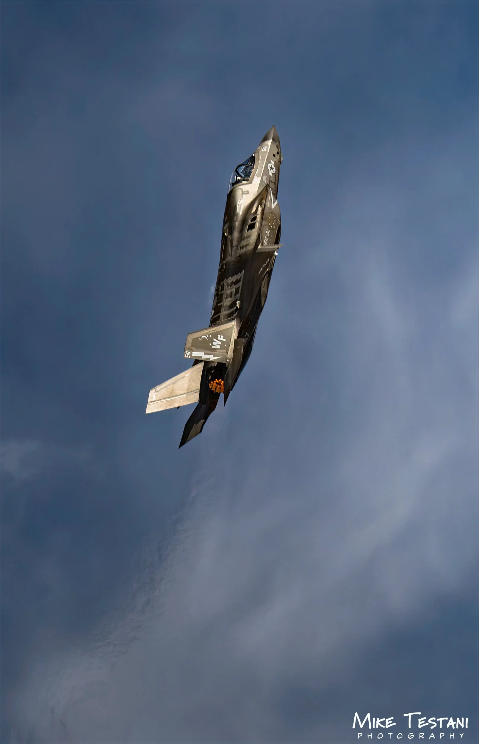 Fighter jet flying in a cloudy sky with the photographer's signature 'Mike Testani Photography' at the bottom right.
