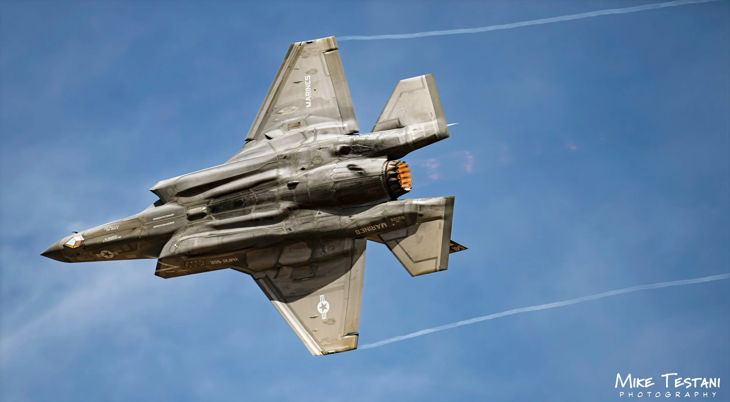 A military fighter jet flying in clear blue sky, leaving contrails behind.