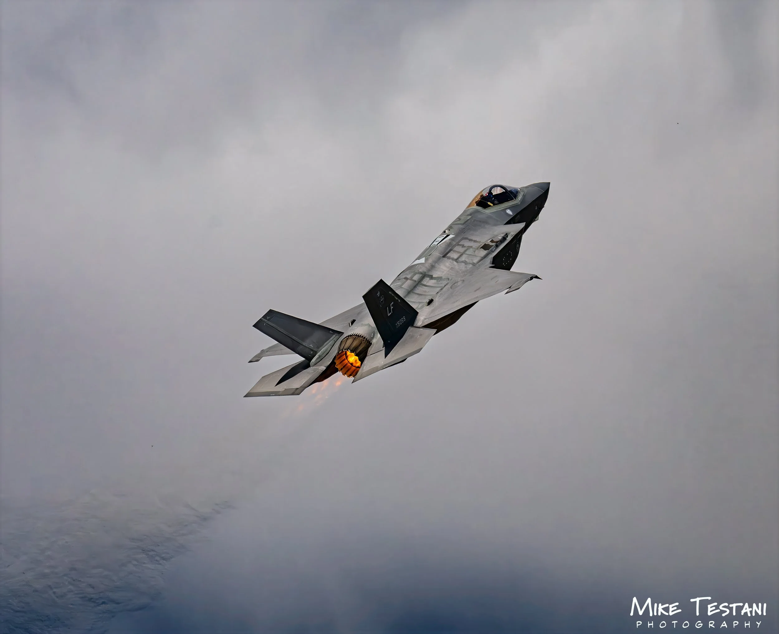 A fighter jet aircraft flying through a cloudy sky over water