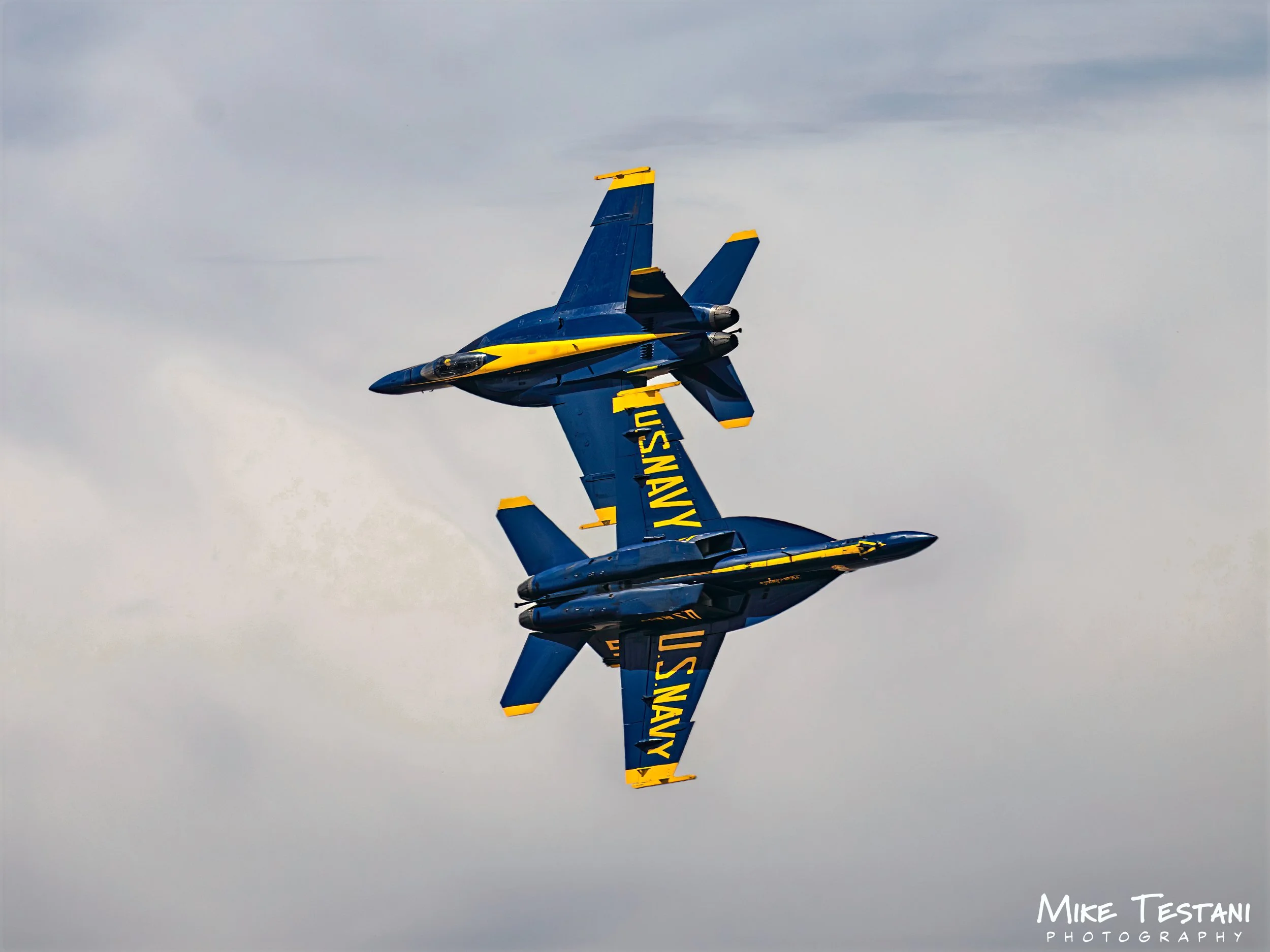 A blue and yellow U.S. Navy Boeing F/A-18 Hornet jet performing an aerial stunt in the sky.