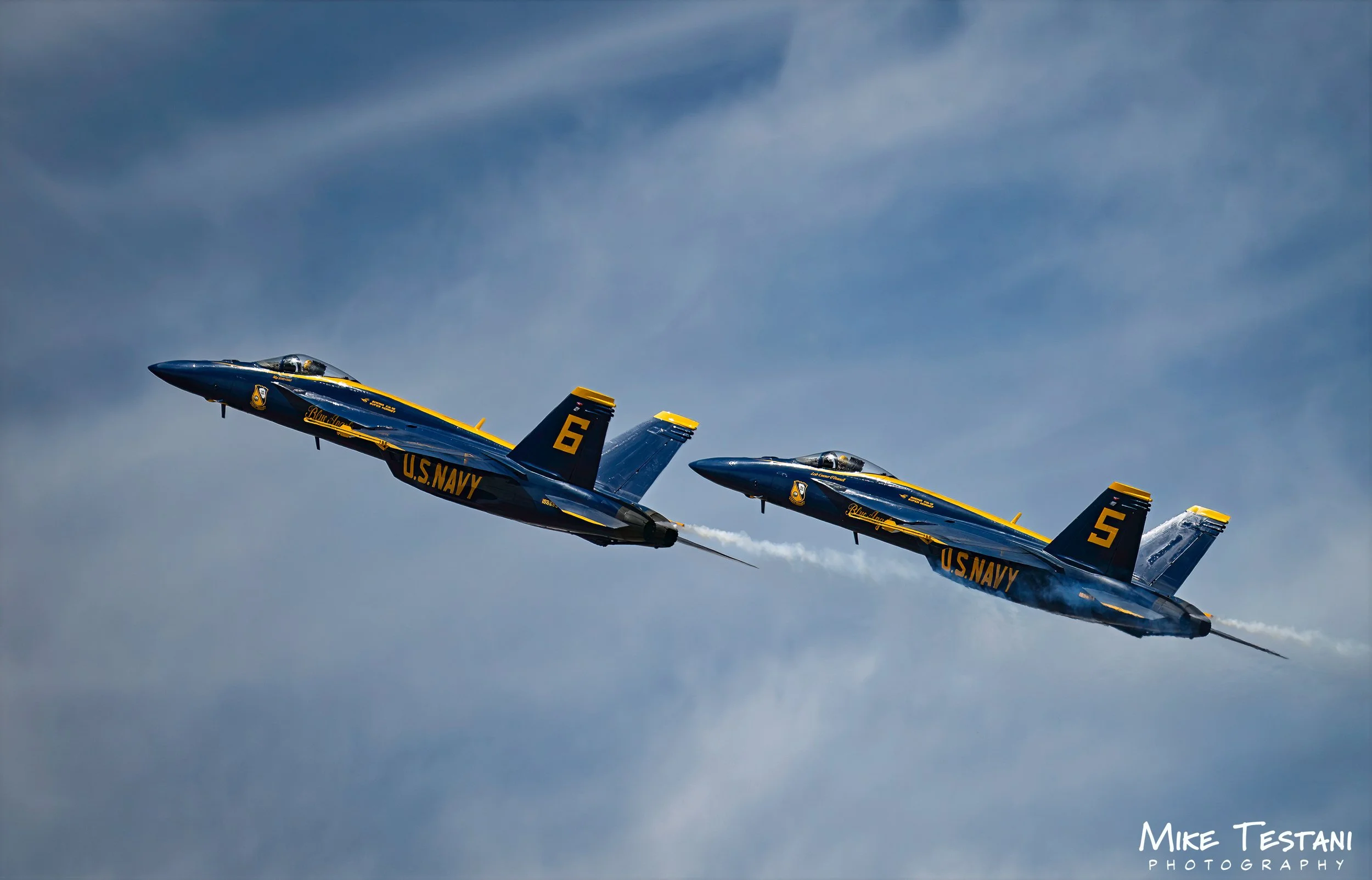 Three U.S. Navy Blue Angels fighter jets flying in close formation through a cloudy sky.