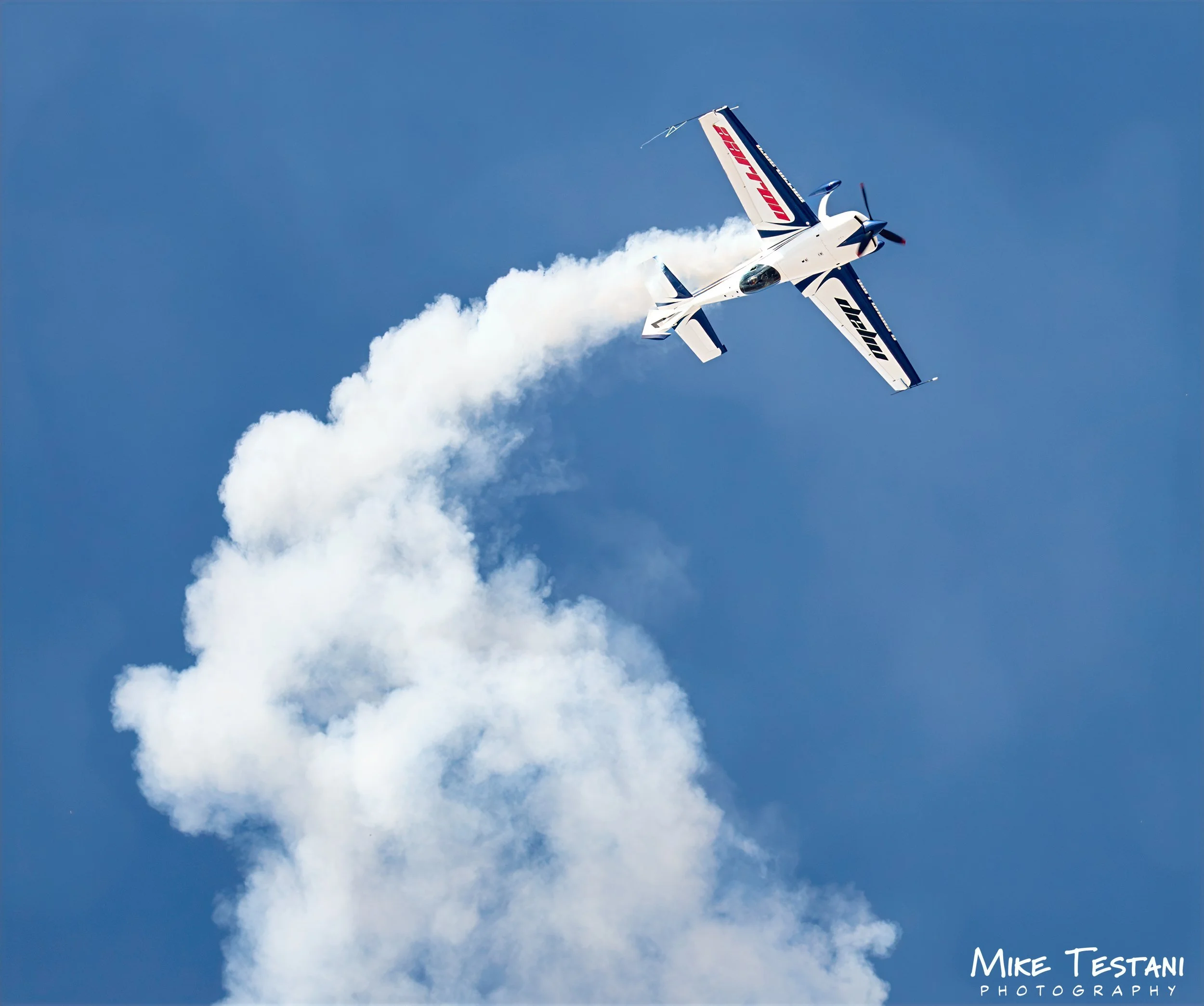 An airplane flying in the clear blue sky, leaving behind a trail of white smoke.