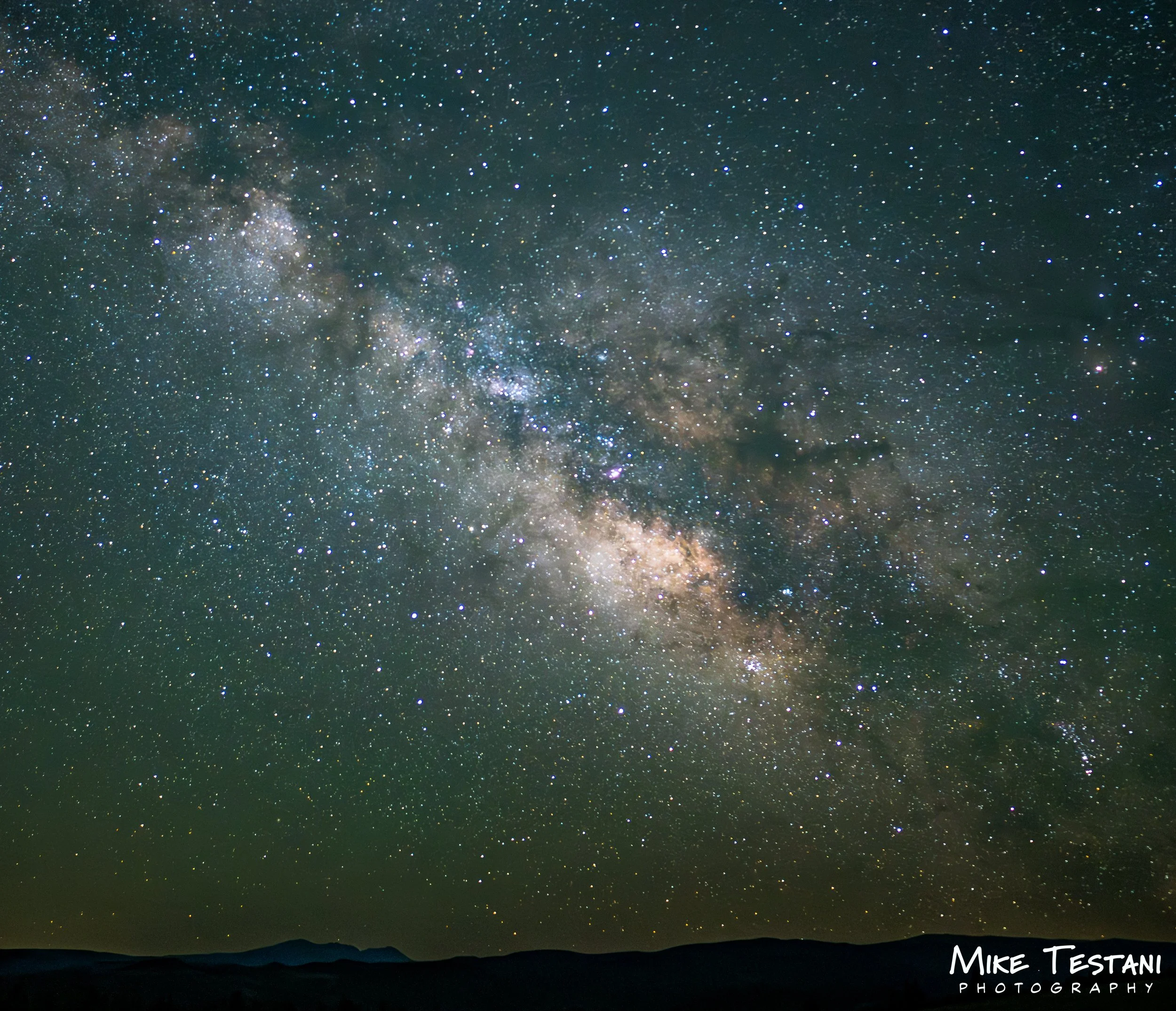 A clear night sky filled with countless stars and the Milky Way galaxy stretching across the horizon, with a silhouette of mountains at the bottom and the text 'Mike Testani Photography' in the corner.