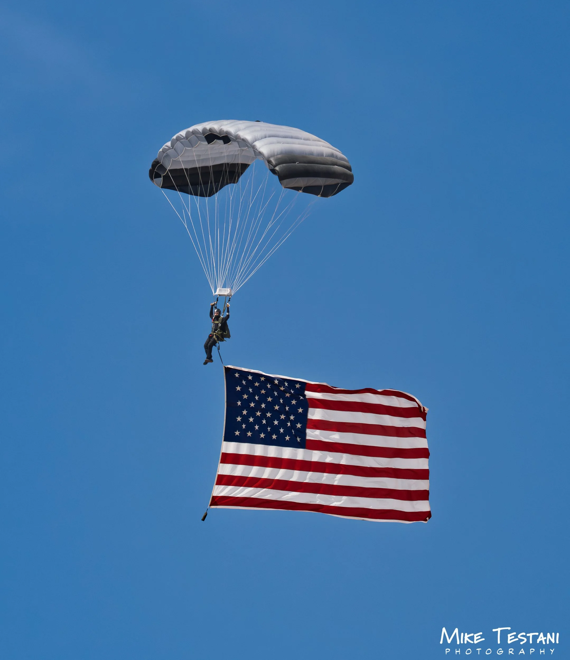 An American flag and a parachutist descending with a parachute in the sky, with the parachutist holding the flag.