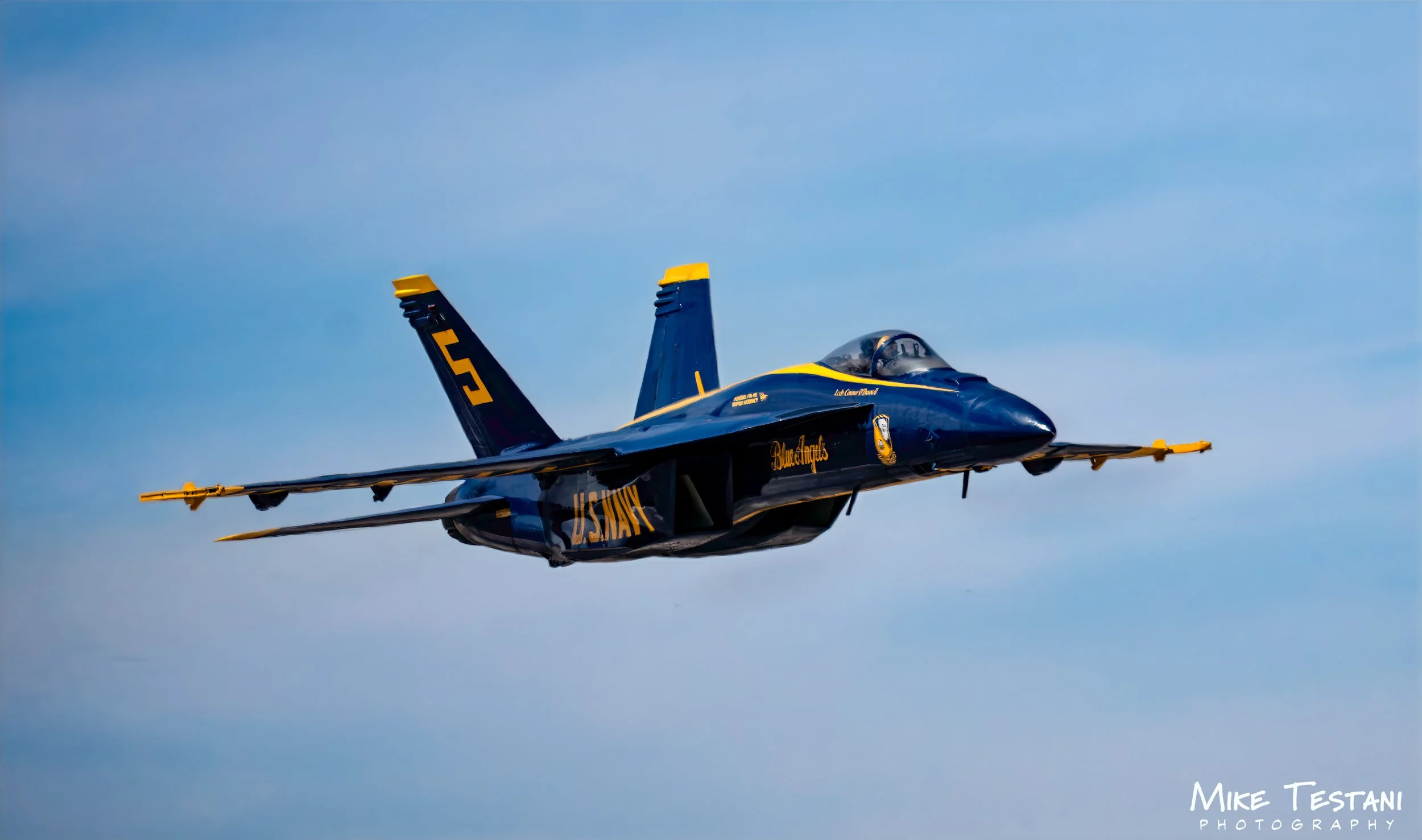A blue and yellow fighter jet flying in the sky with a clear blue background.