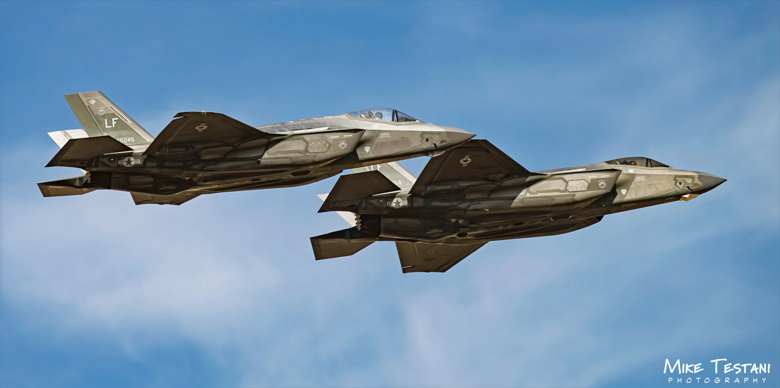 Two fighter jets flying in formation against a blue sky.