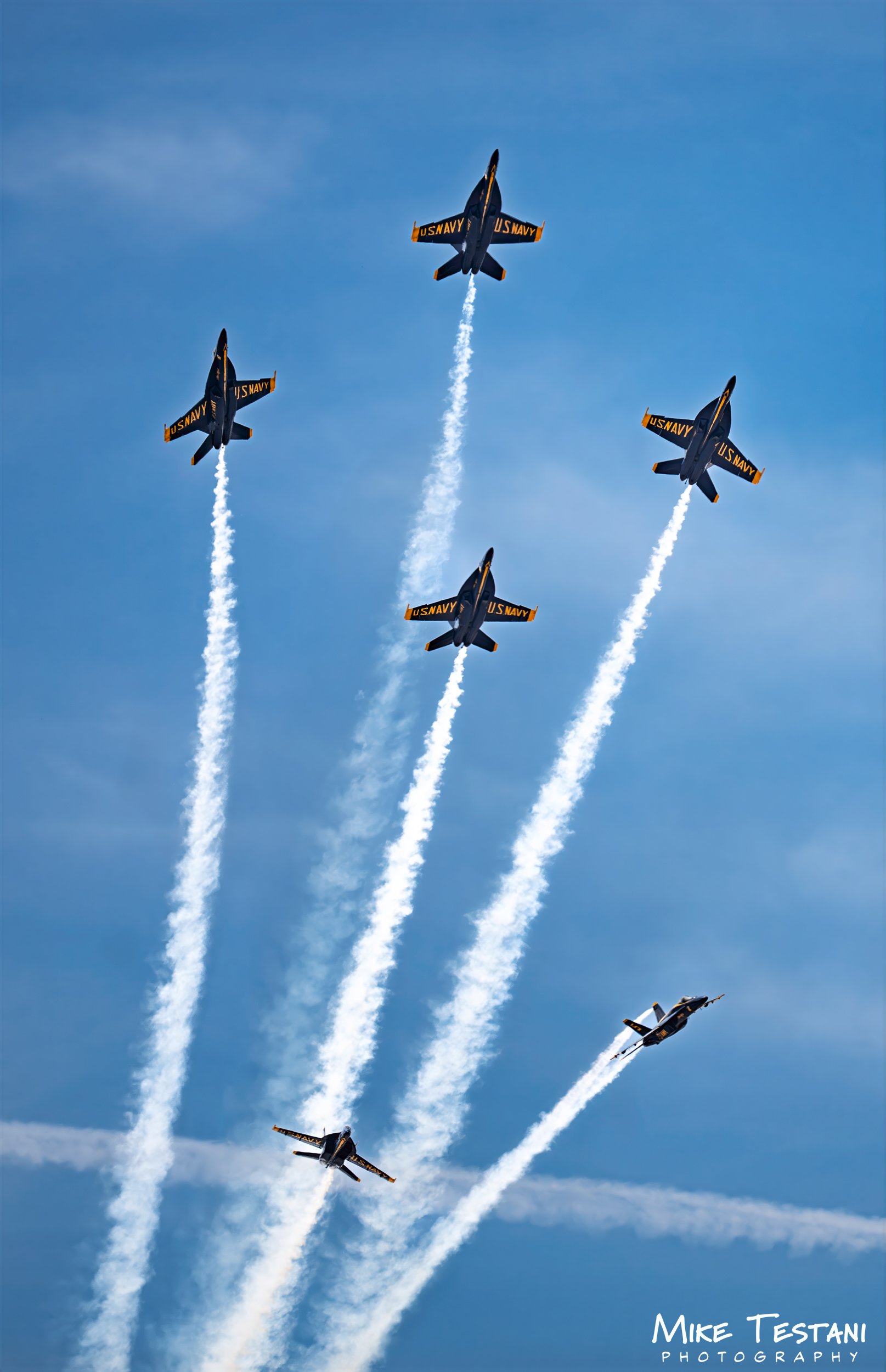 Eight US Navy jets flying in formation through a blue sky, leaving white smoke trails behind them.