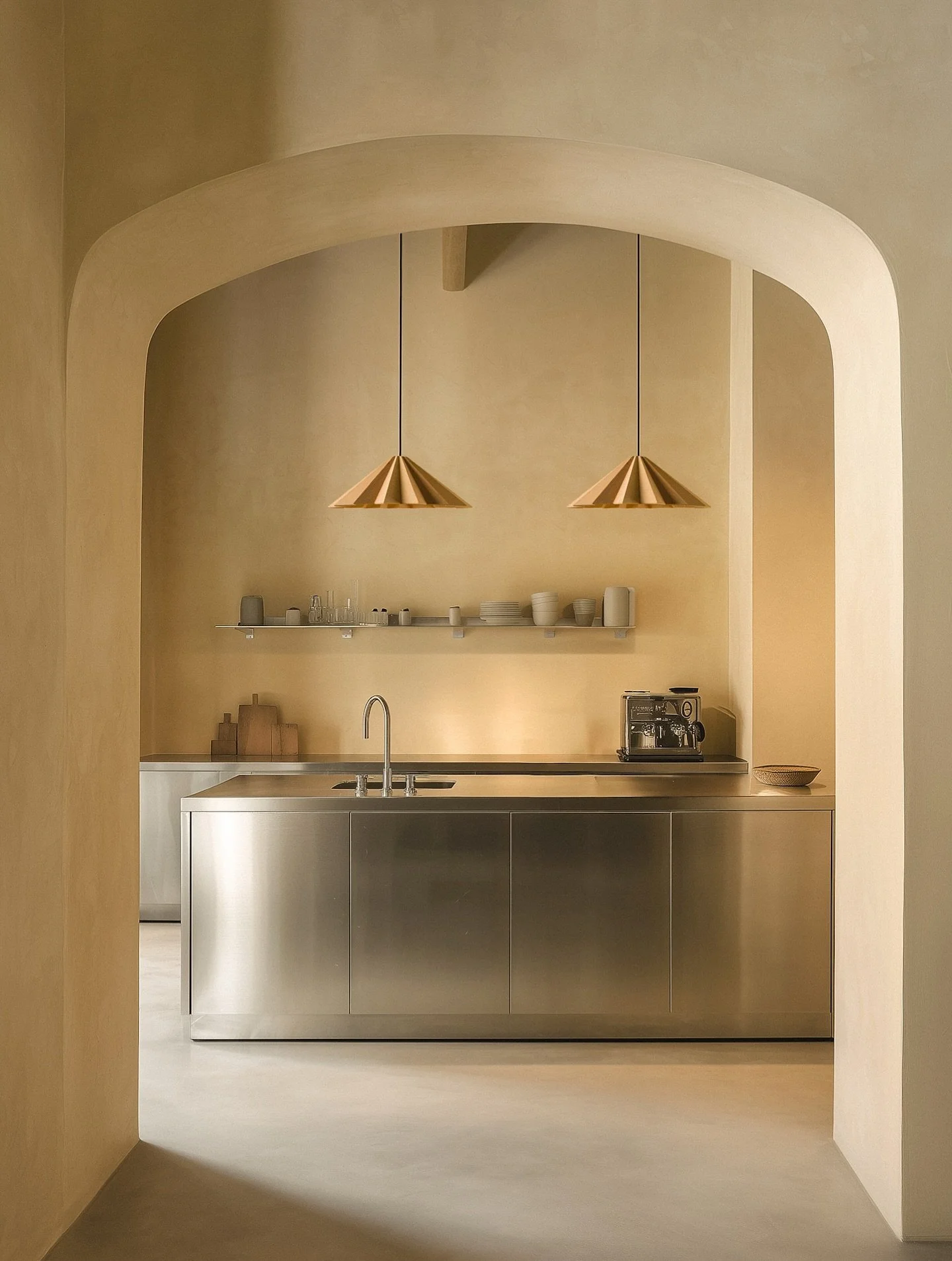 Framed by sunlit arches and the gentle patina of plaster walls, this kitchen&rsquo;s cool steel surfaces meet the warm, sculptural presence of our wooden Stratus lamps. A composition that feels both rooted in tradition and attuned to contemporary liv