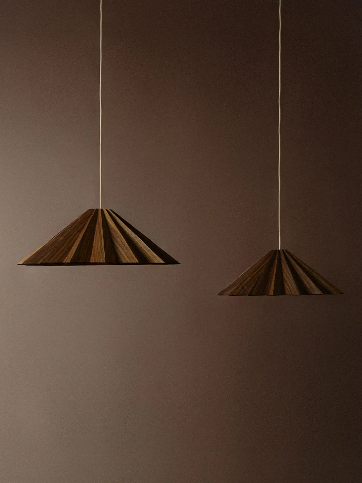 Where form meets a new material, a different mood emerges. Stratus in walnut carries a layered tactility, the folds catching light in slow, earthy gradients. The silhouette is unchanged, yet its presence feels distinctly transformed &mdash; quieter, 