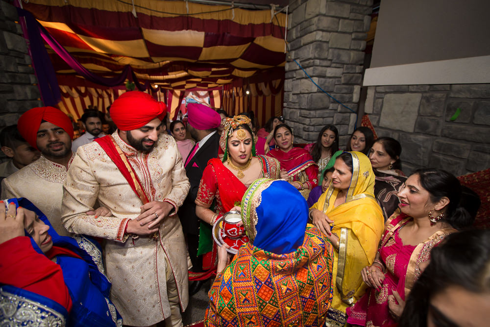 Holding a glass of a glass of water in her hand, which she circles 3 times around her bahu and then offers it to her to drink, as a symbol of her acceptance and blessing as her newest daughter.