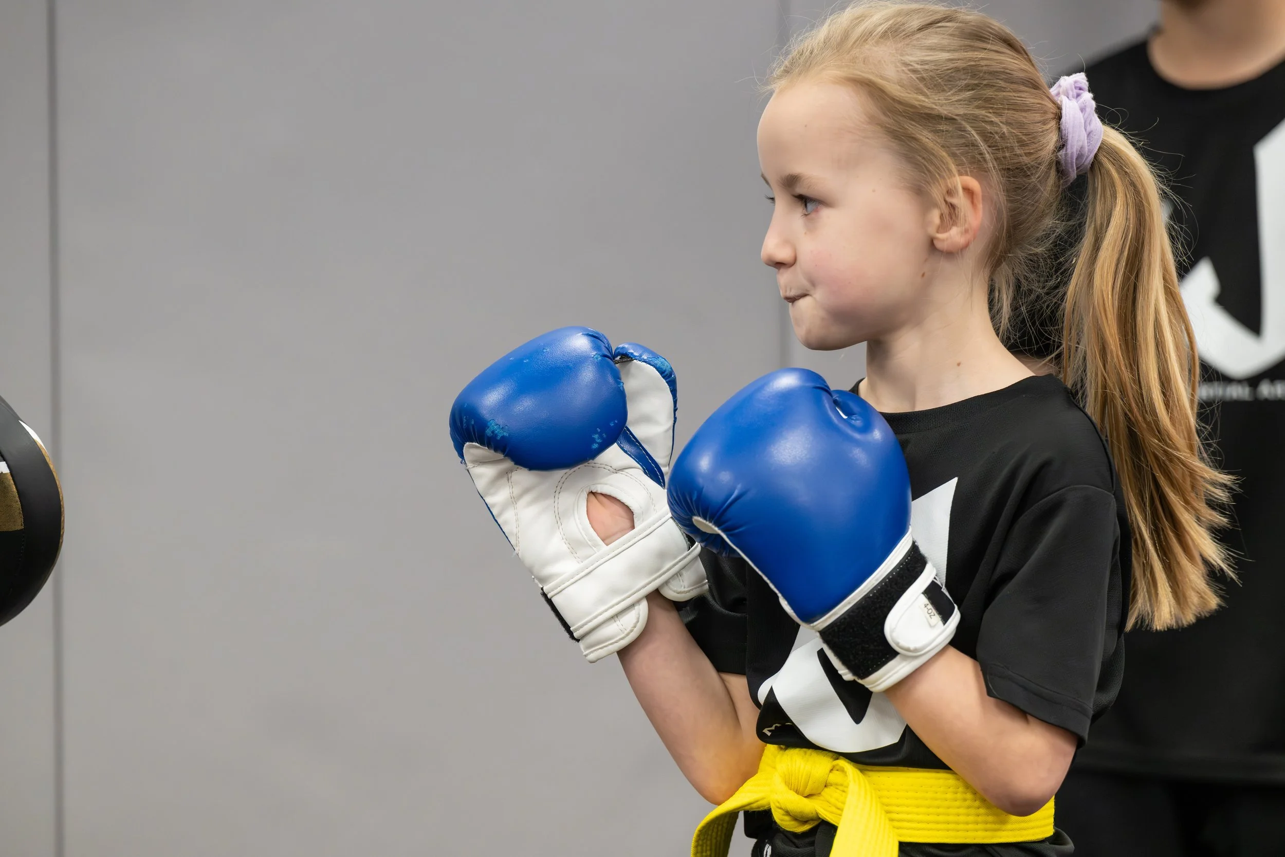 Young girl with a yellow belt practicing boxing in gloves, standing in a fighting stance with her fists up.
