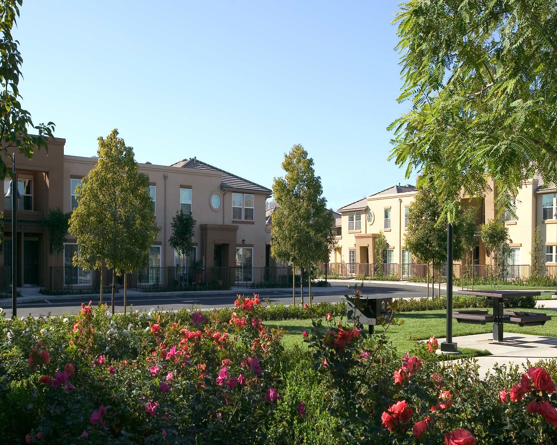 Buildings are kept small and oriented to green spaces to belie the density while other apartments from the public streets with entry doors and front porches. The continuing struggle to balance privacy vs. community has been addressed by the use of townhouses, the almost complete elimination of units facing units and a north/south pedestrian walk that knits the site together while passing through a Village Common.