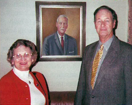 Marion and George W. Chapman Jr. stand before a portrait of George W. Chapman that hangs on the wall of The Chapman Library at the International Headquarters