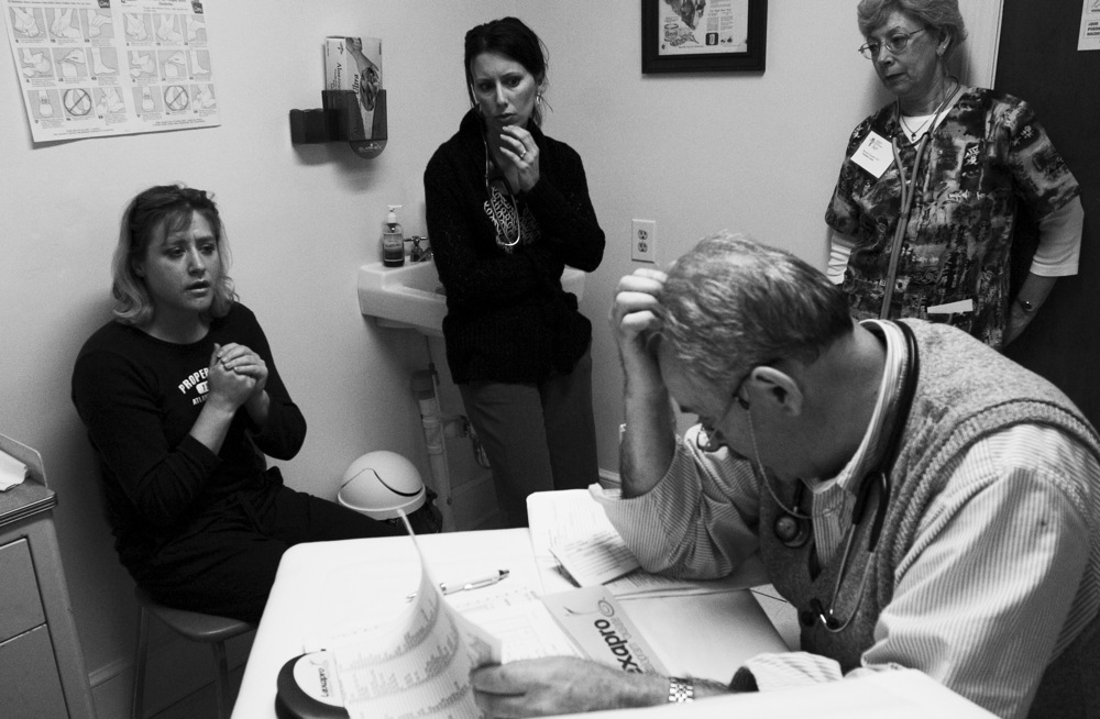 Dr. Stover scratches his head as he listens to new patient Laura, left, describe her daily regiment o keep her diabetes in check. Nurse Practitioner Blessing, center, is learning the ropes to become a volunteer provider so that the clinic can open an additional night during the month. Nurse Lipinski, right, waits for the doctor’s instructions on how to proceed with Laura’s prescriptions.