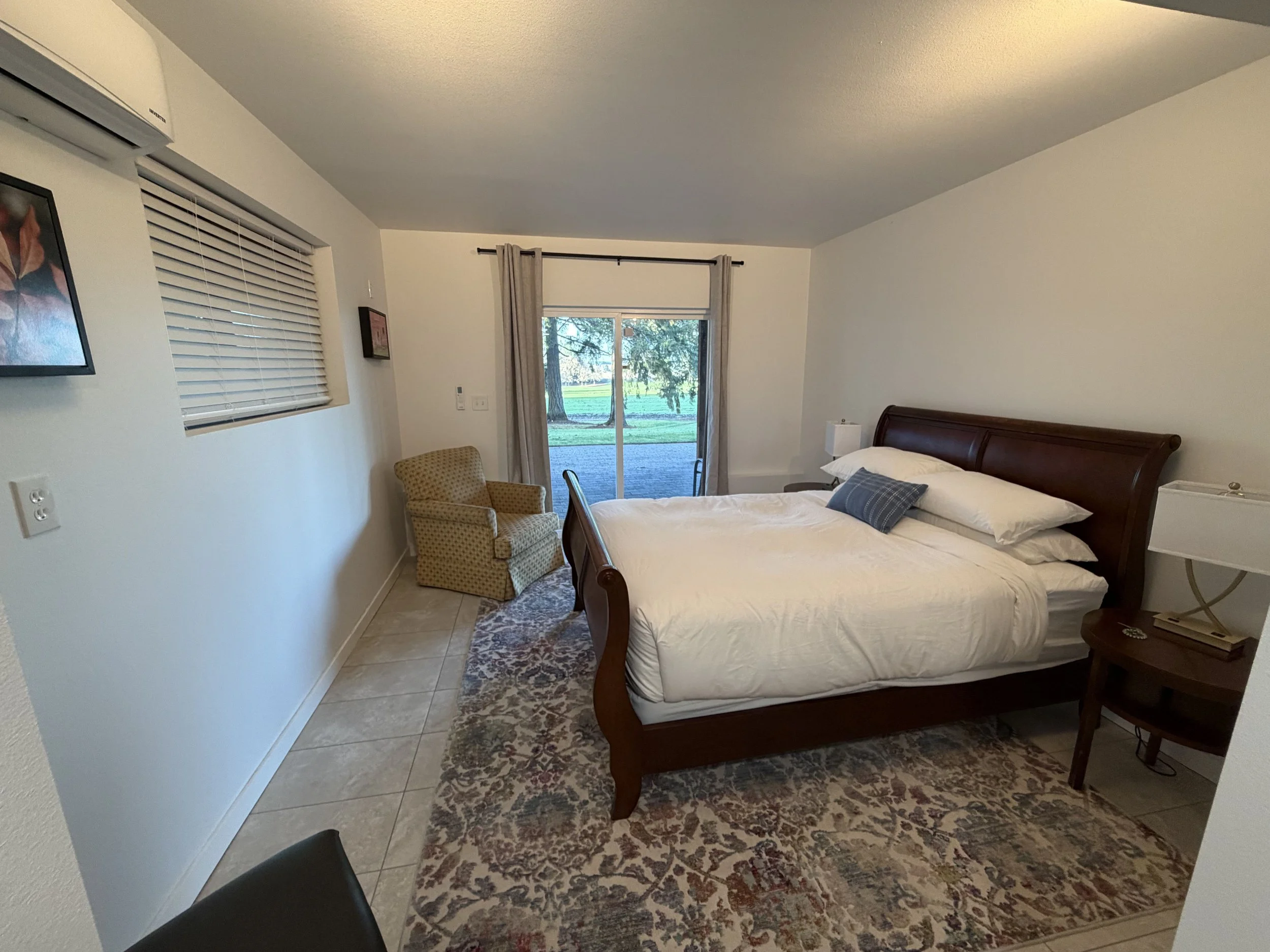 Bedroom with a bed, a nightstand, a window, and a sliding door opening to a view of trees outside.