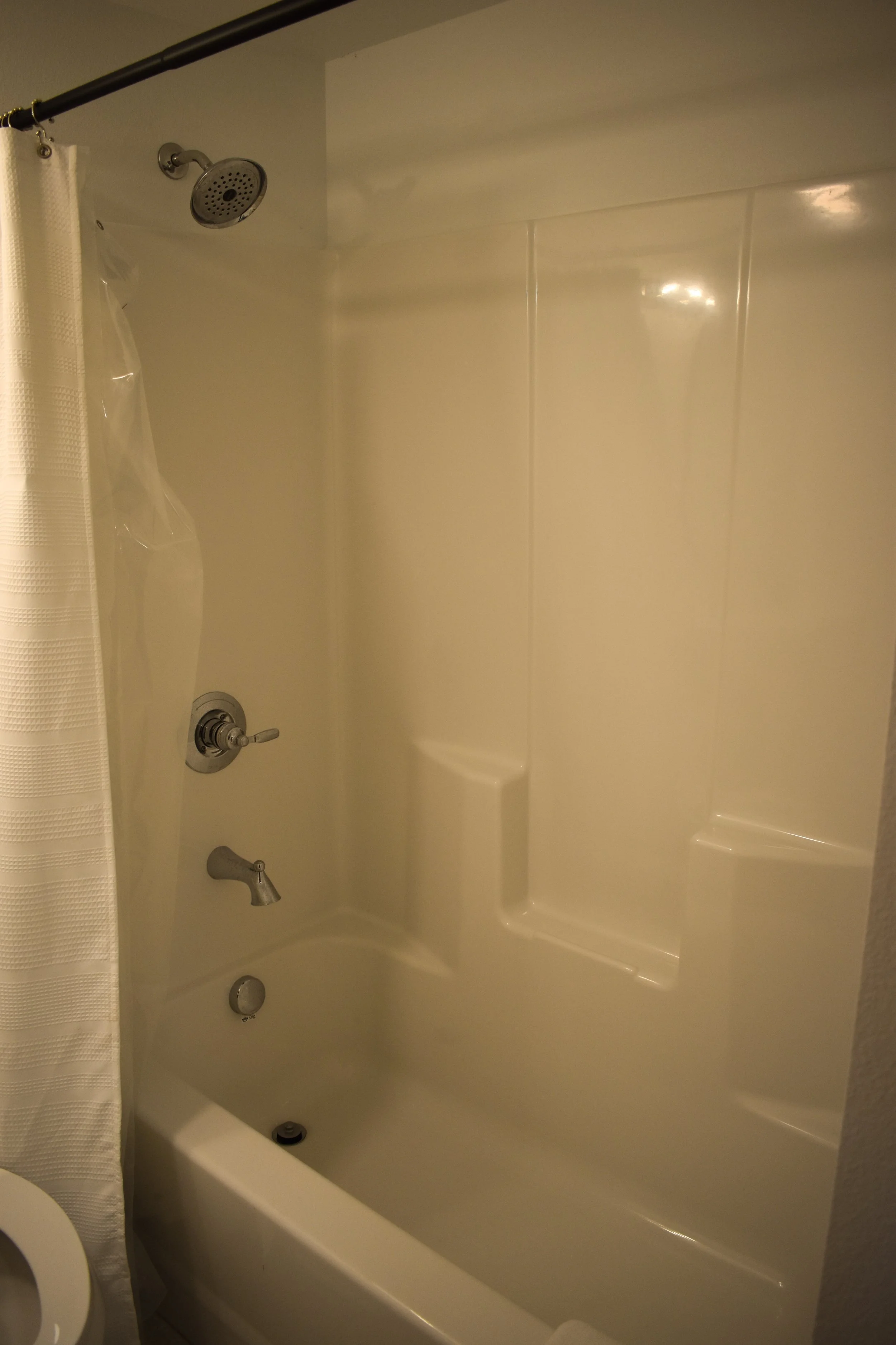 Bathroom bathtub with a showerhead, faucet, and a shower curtain on the left side.