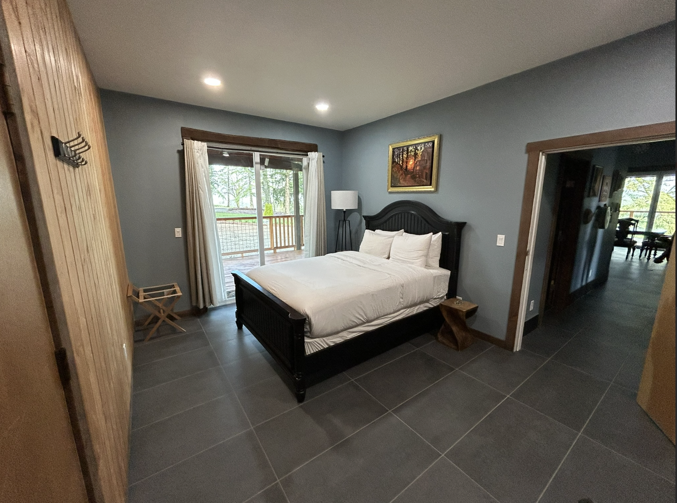 Bedroom with a bed, nightstand, floor lamp, and a painting on blue walls, with sliding glass door leading to a balcony.