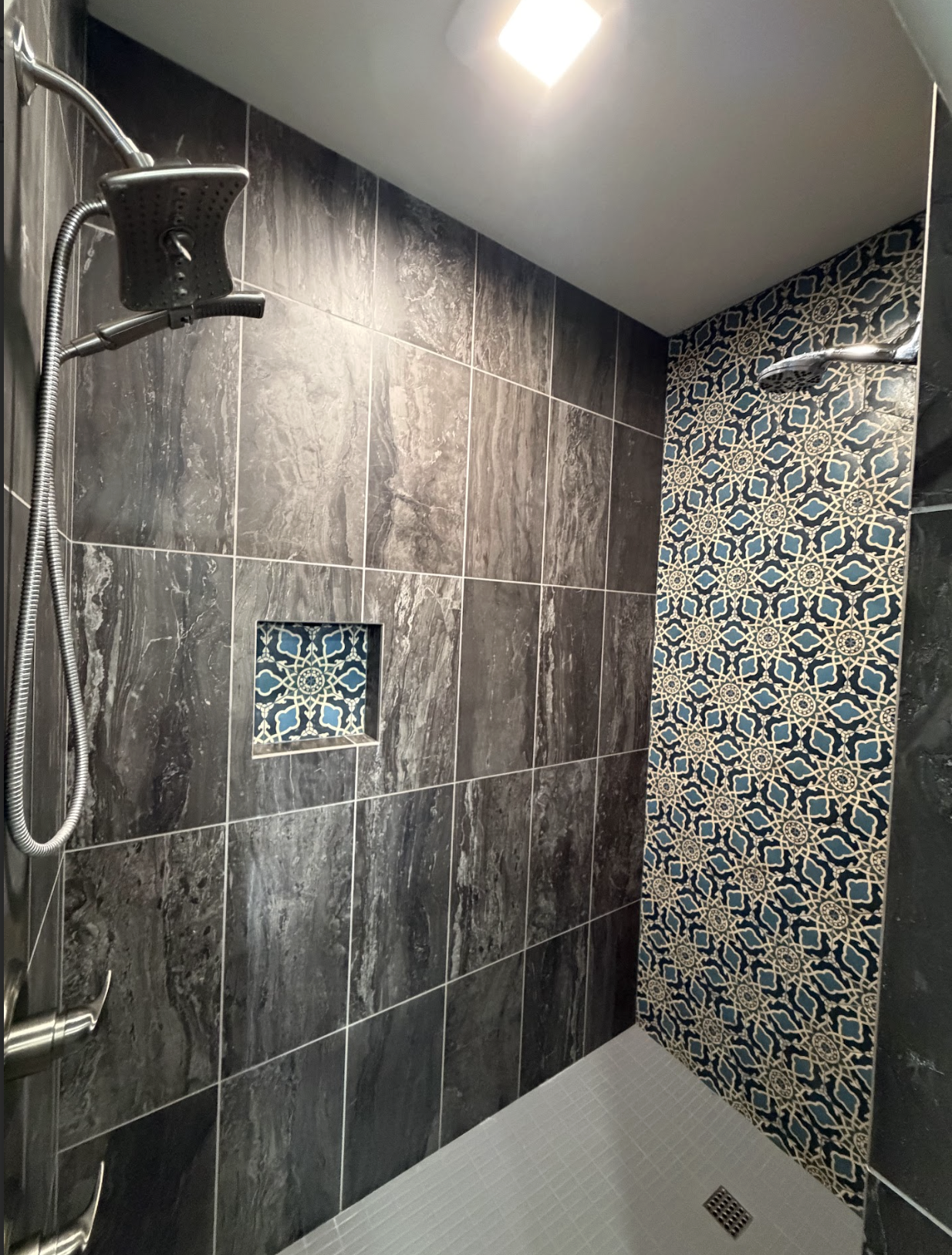Modern shower with dark gray marble tiles, a decorative blue and beige tile accent wall, a built-in niche, and a ceiling light fixture.