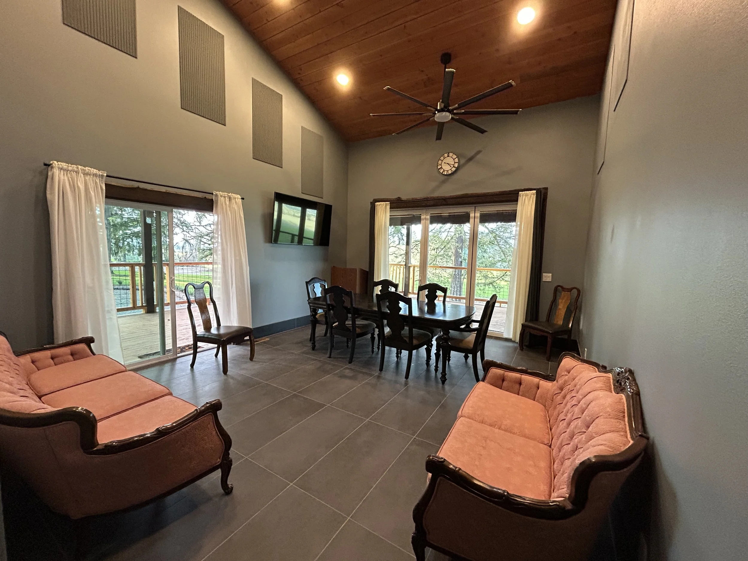 Living room with pink vintage sofas, dark wood dining table, chairs, large windows with white curtains, and a ceiling fan.