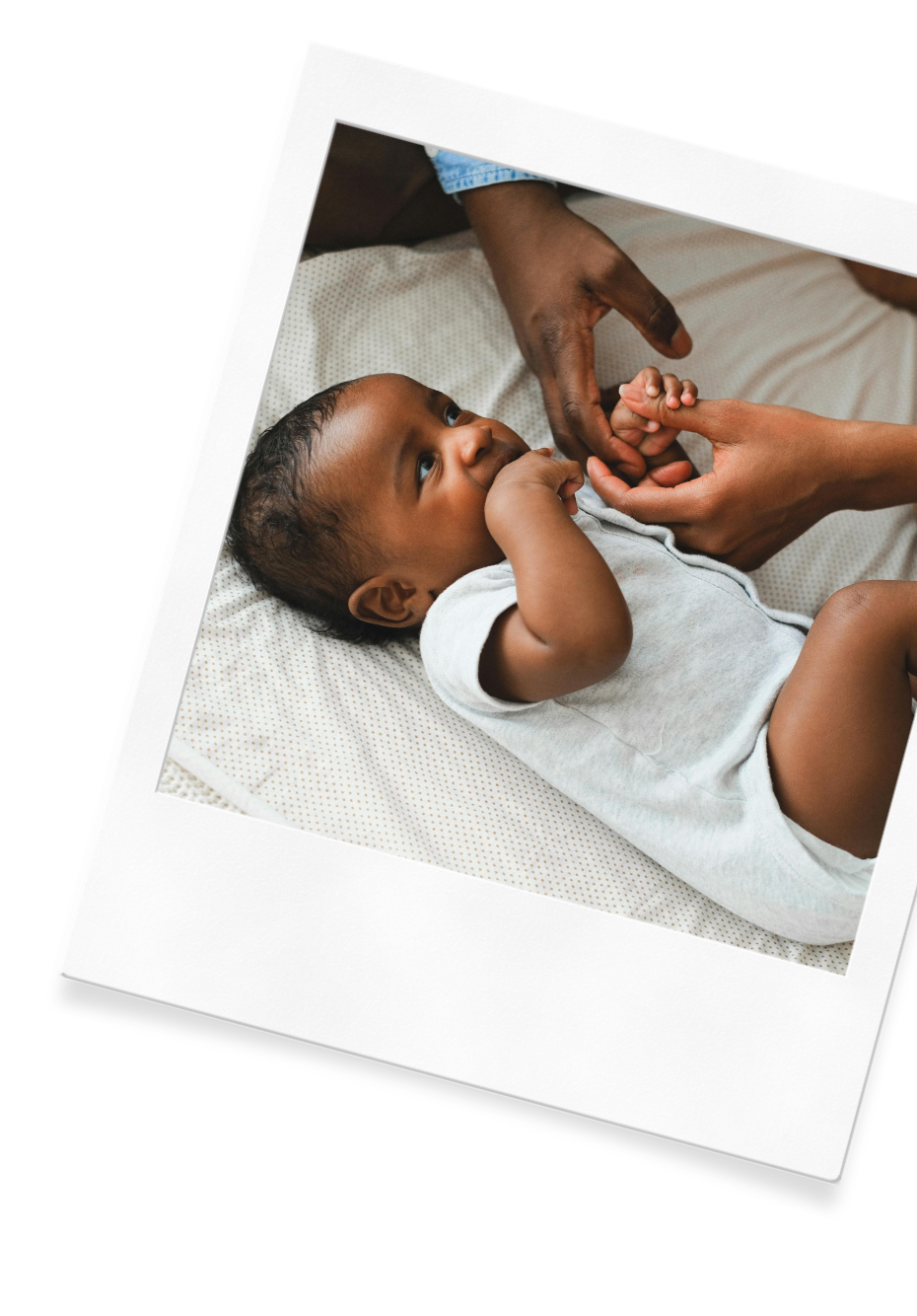 A mother and father hold their baby's hand while they lay him down to sleep.