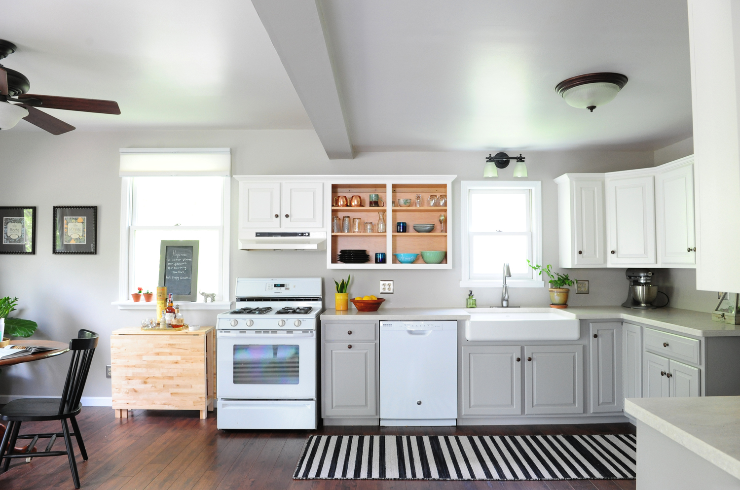 Simple, affordable kitchen update. Cabinets painted; vinyl floors swapped to plank laminate; drop-in stainless steel sink replaced with an apron farmhouse sink; laminate countertops upgraded to solid surface. The before can be found here . 