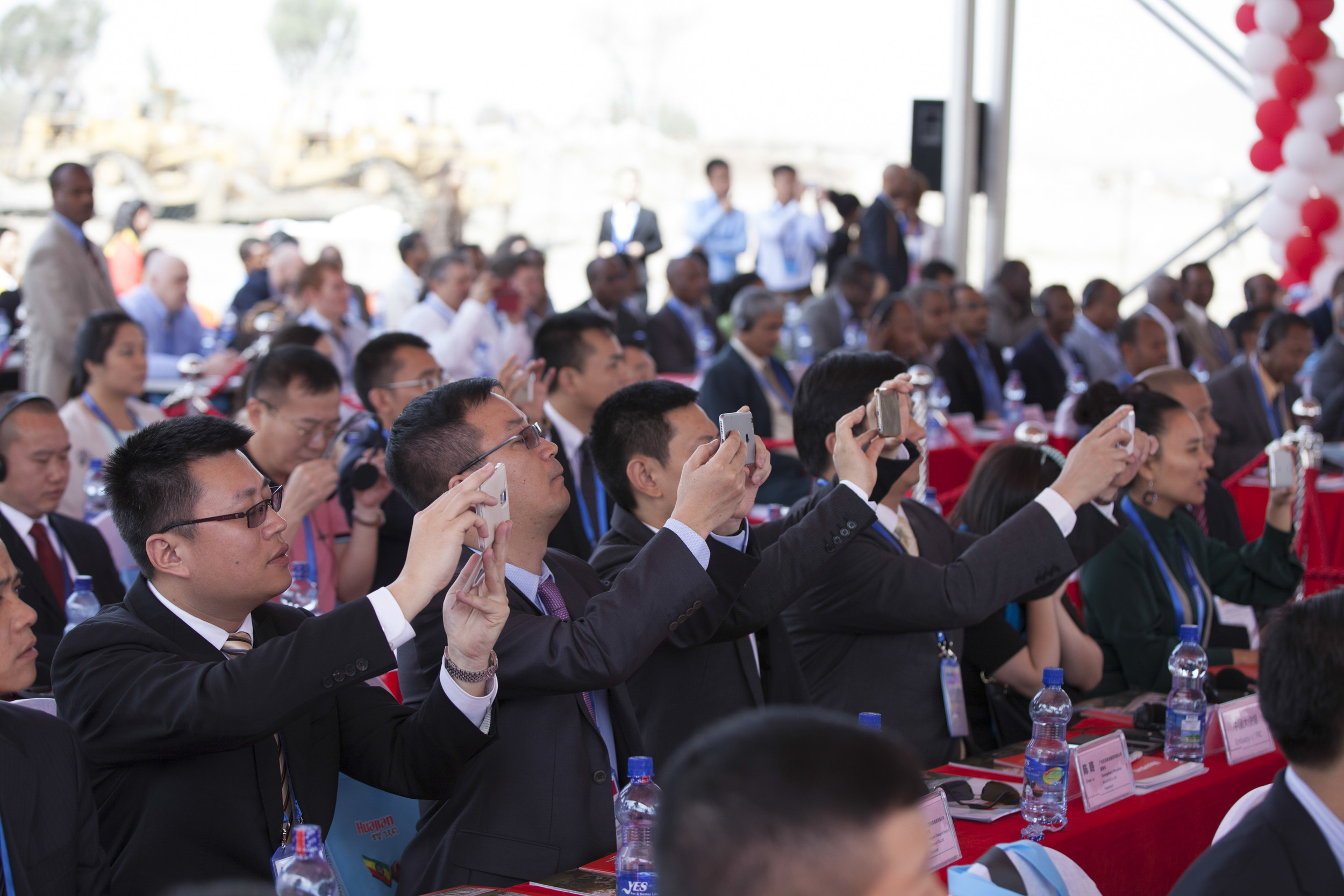  Chinese businessmen are pictured taking photos with their phones during the opening ceremony for the groundbreaking of the Ethiopia-China Dong Guan Huajian International Light Industrial Zone outside of Addis Ababa on 16 April 2015. AFP Photo / Zach
